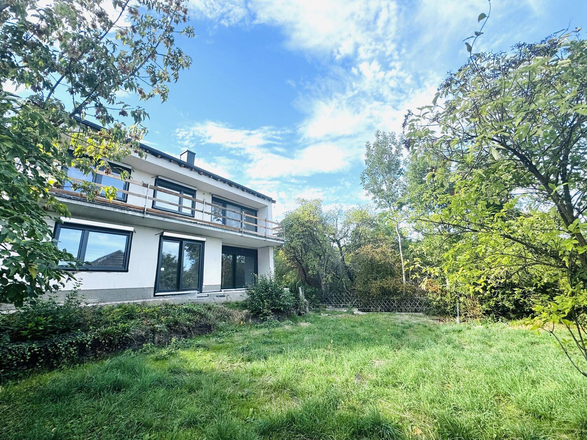 Rückseite eines modernen Hauses mit Balkonen und einem weitläufigen Rasenbereich im Garten.