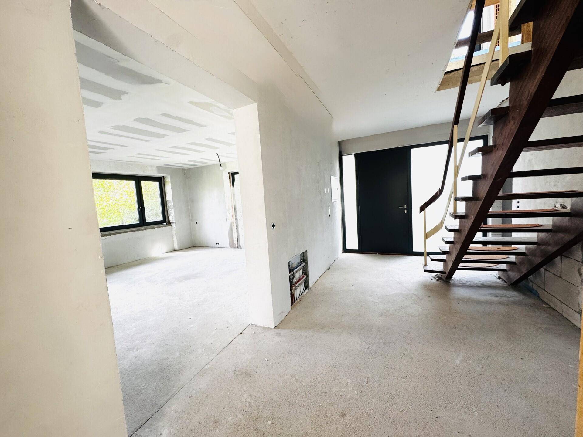 Eingangsbereich im Rohbau mit Betonboden und einer unfertigen Treppe.