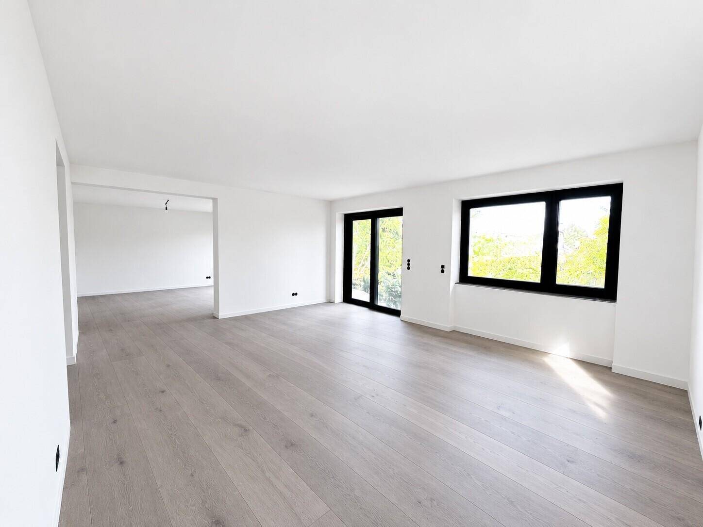 Heller, leerer Wohnraum mit modernem Holzboden und großen Fenstern, die viel Licht hereinlassen.