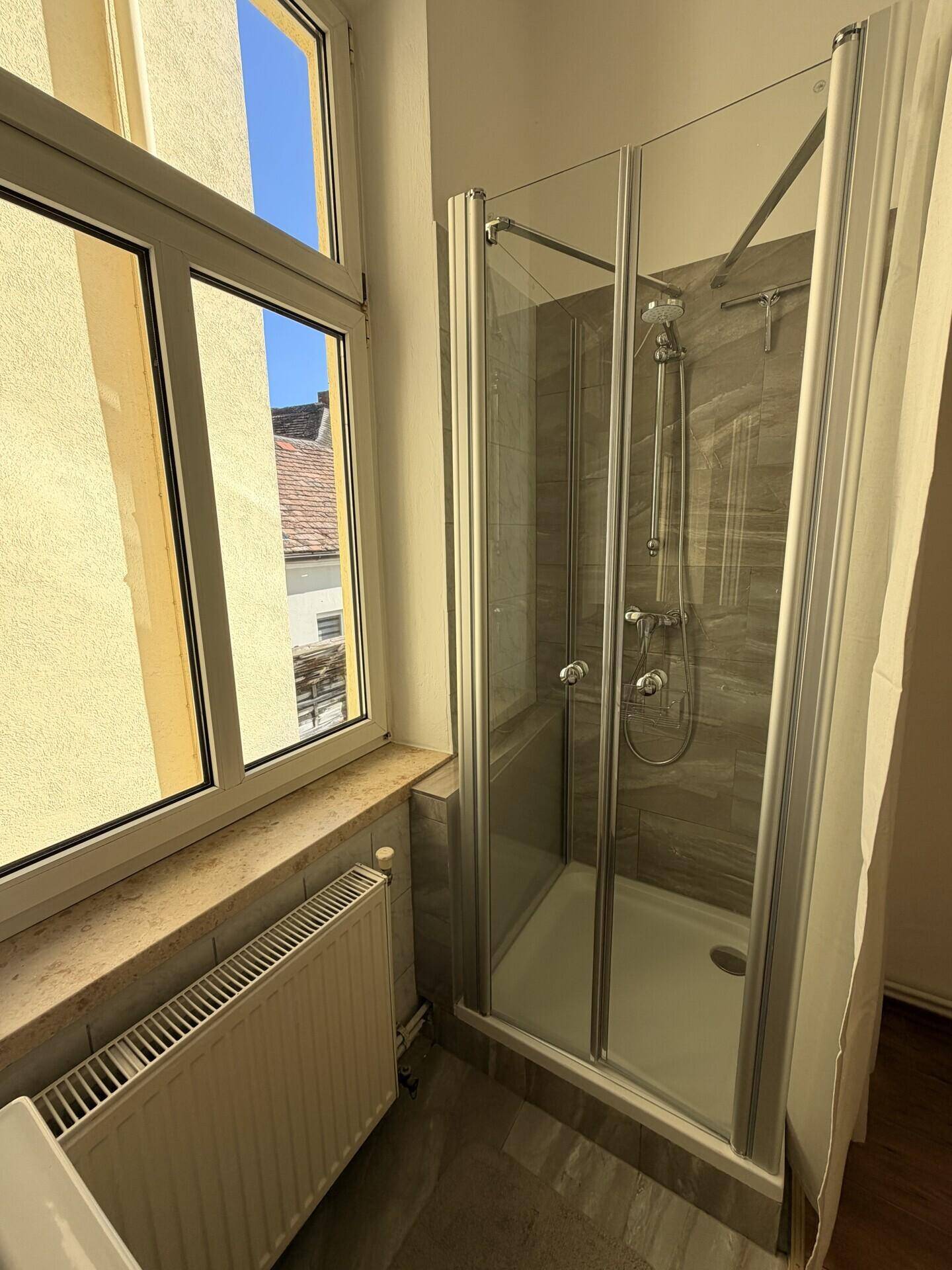 Modernes Badezimmer mit Duschkabine, Fenster und Heizkörper, hell und funktional gestaltet.