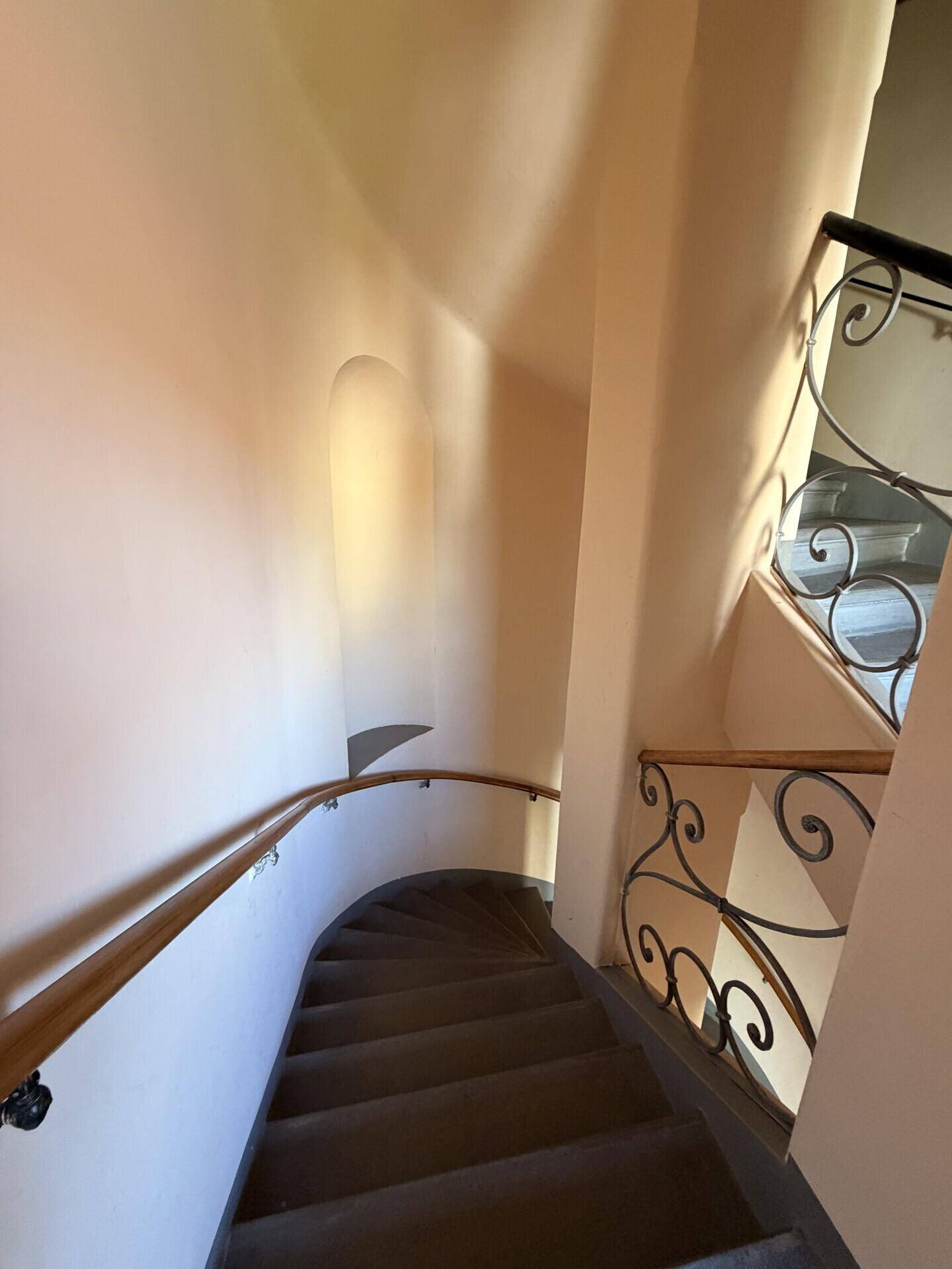 Geschwungene Treppe mit schmiedeeisernem Geländer und Holzhandlauf, führt zu den oberen Etagen.