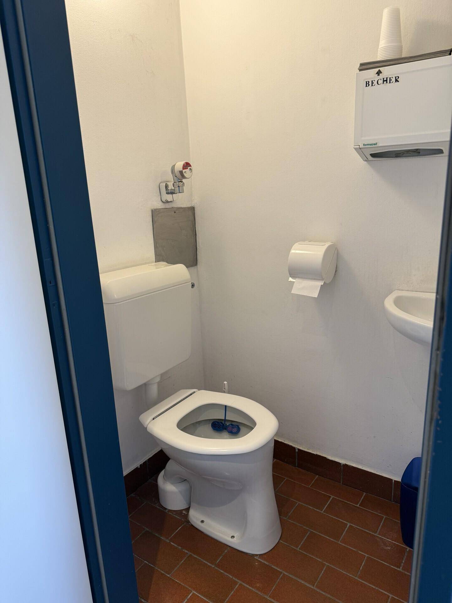 Separate Toilette mit Terrakotta-Fliesenboden, WC und kleinem Waschbecken.