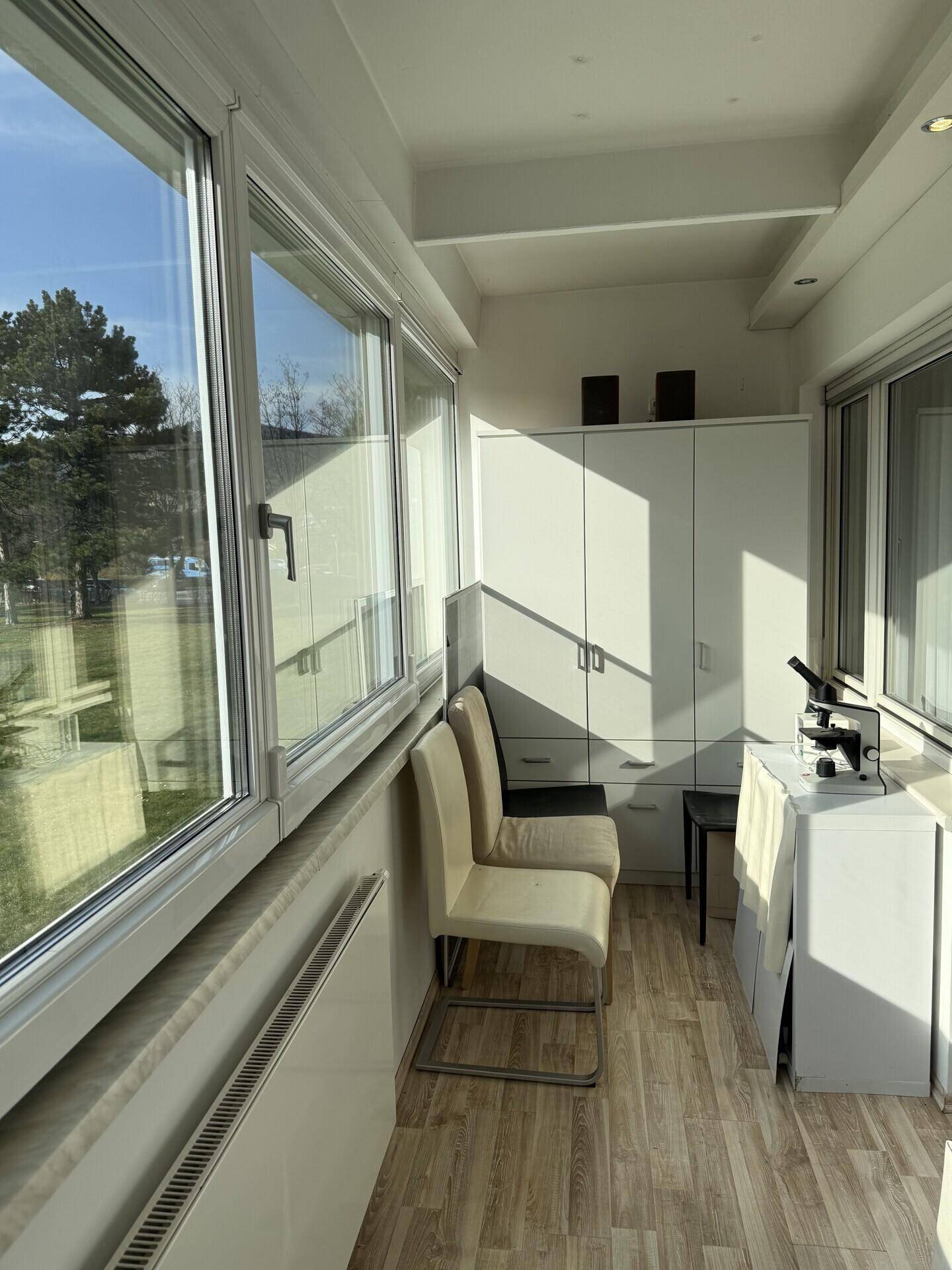 Heller, verglaster Balkon oder Wintergarten mit Schränken, Stühlen und weitem Ausblick.