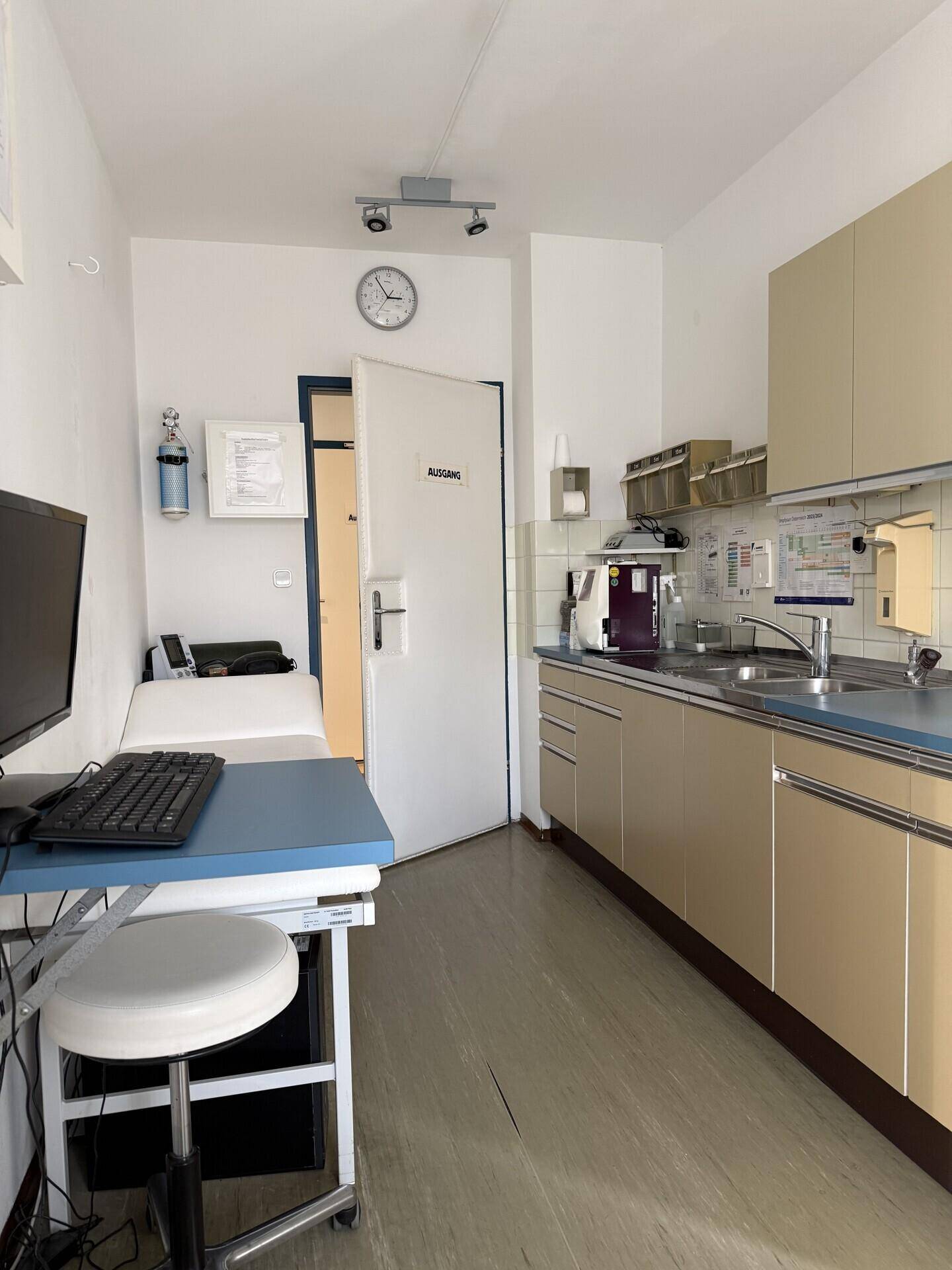 Kleine Küchenzeile mit Spüle, beigen Schränken und Arbeitsfläche in einem Büroraum.