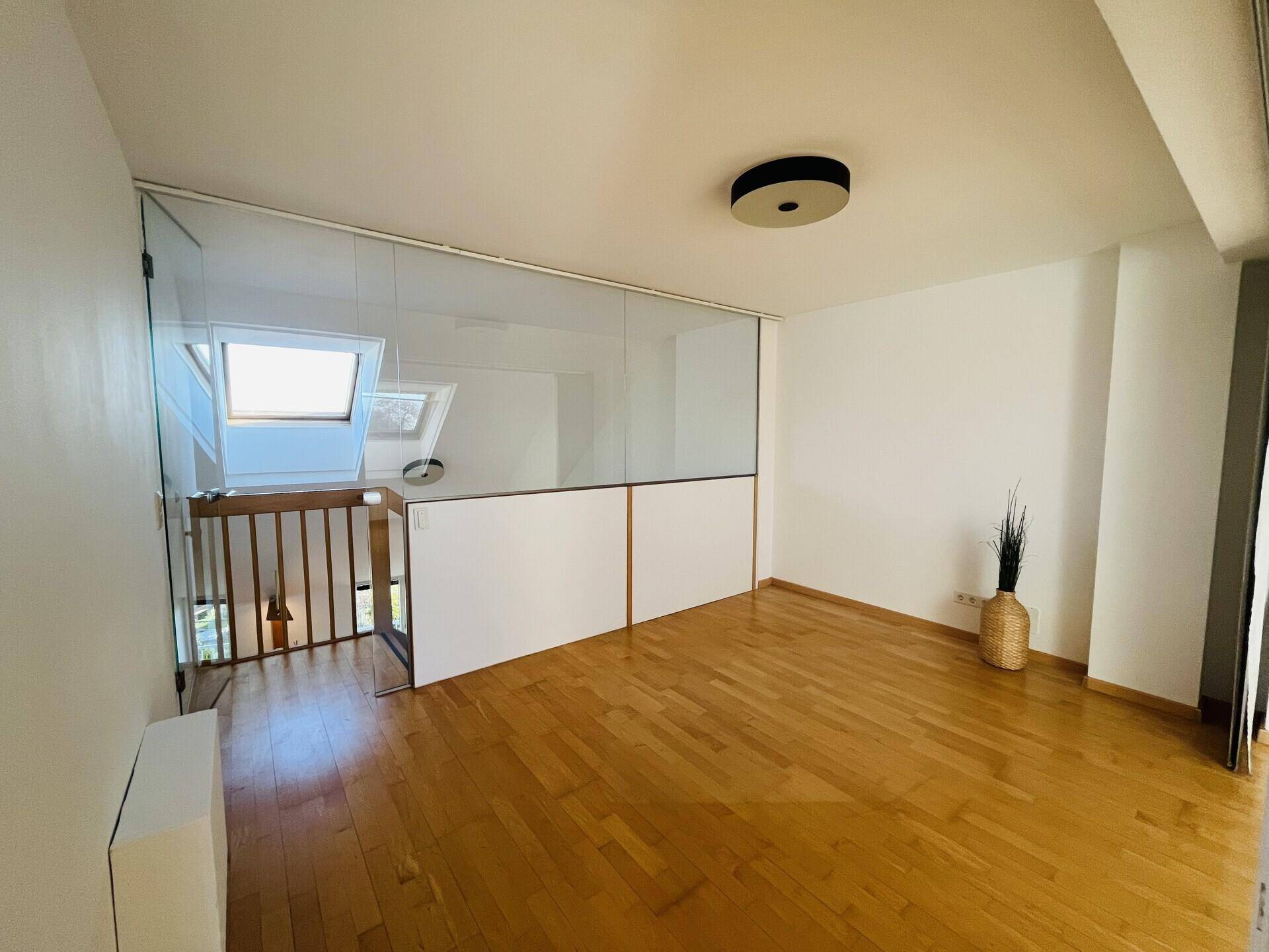 Offener Raum im Obergeschoss mit Glasabtrennung und Holzboden.
