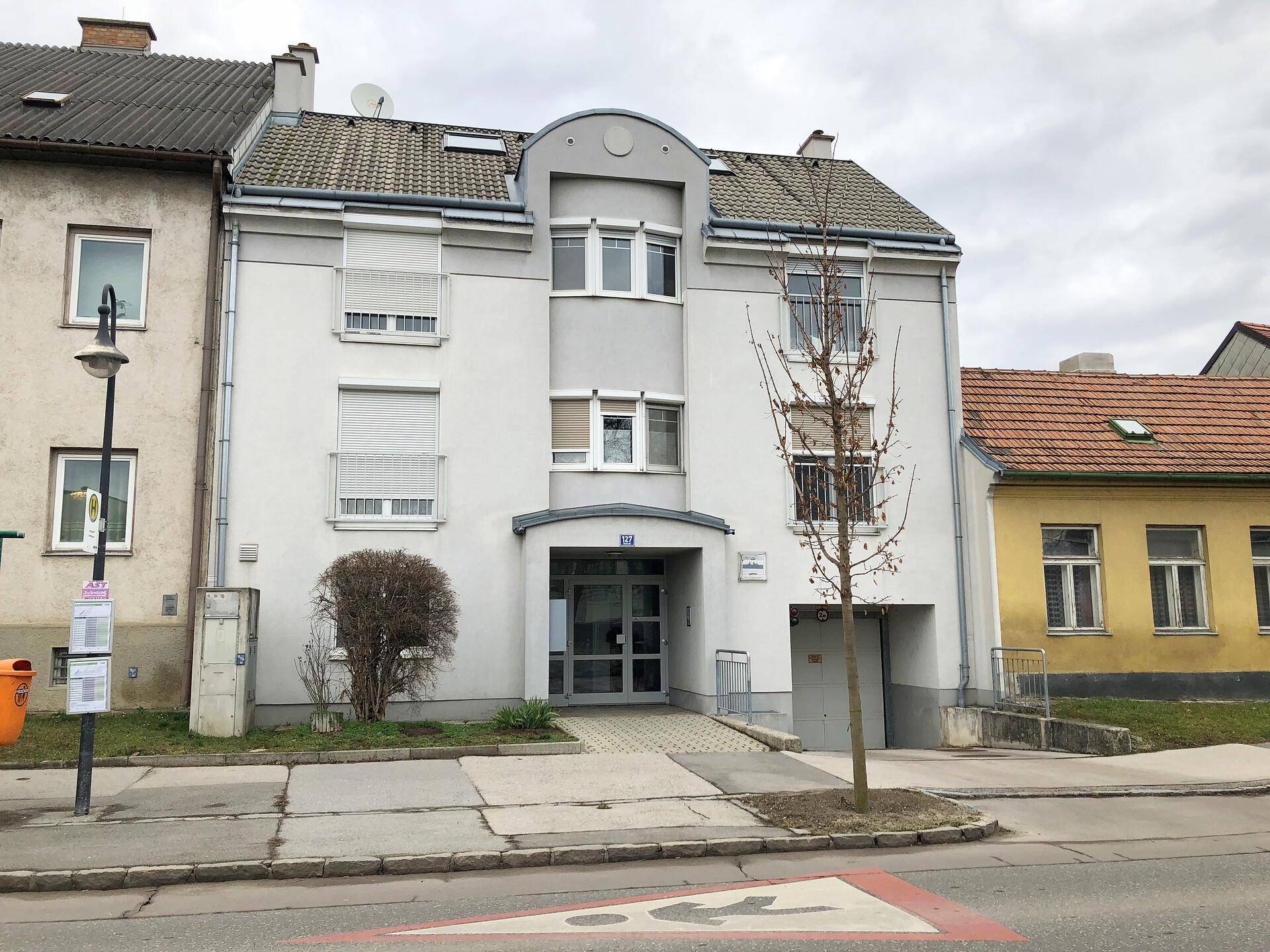 Moderne Gebäudefassade mit Eingangsbereich, Rampe und Rollläden an den Fenstern.