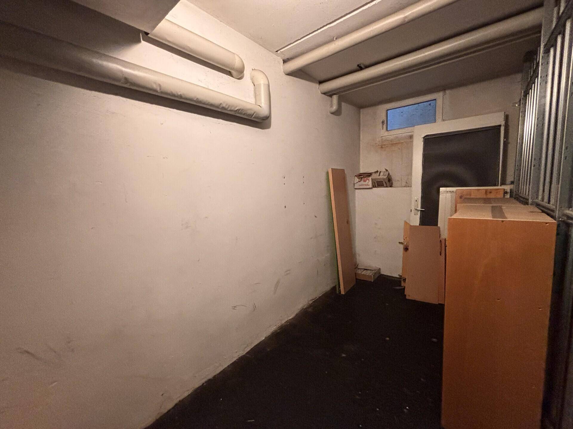 Kellerraum mit einfachen Wänden, Rohren und einem kleinen Fenster.