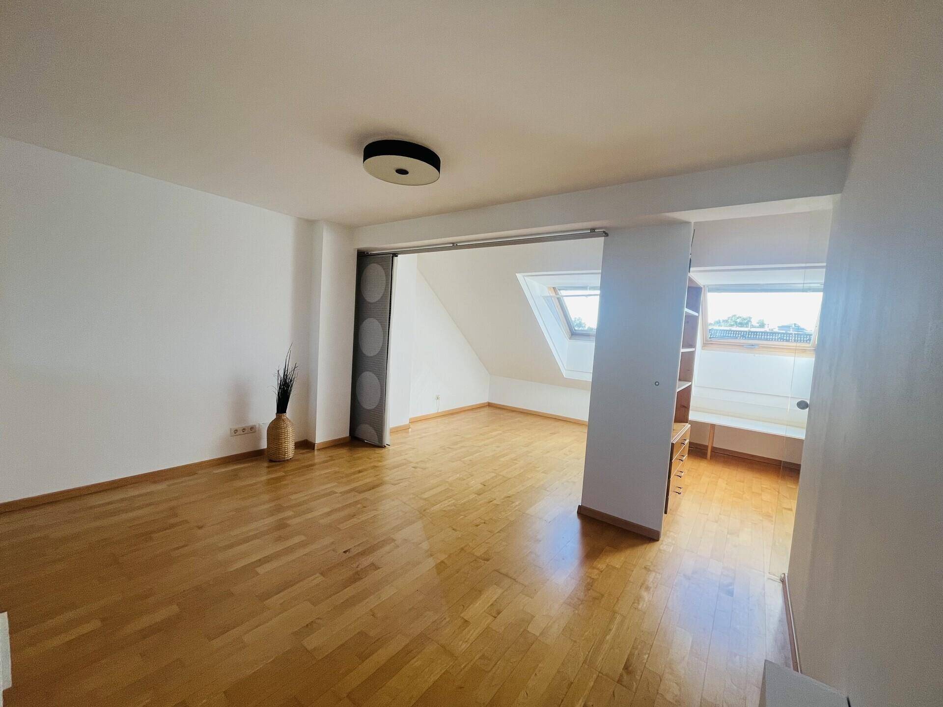Geräumiger Raum im Dachgeschoss mit Holzboden und Dachfenster.