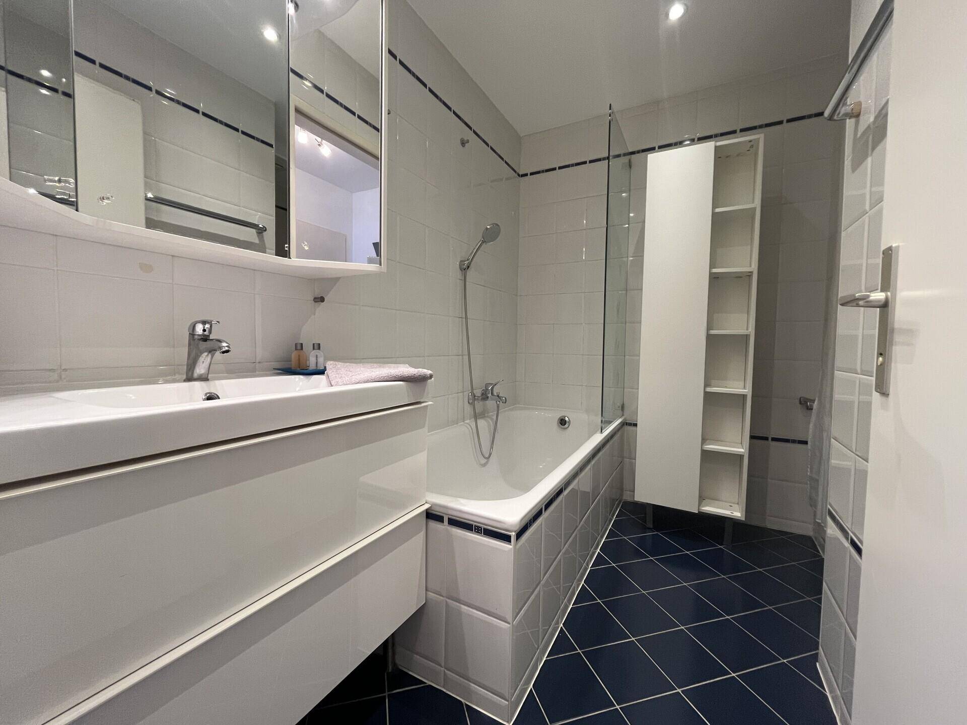 Helles Badezimmer mit Badewanne, Waschbecken und blauen Bodenfliesen.