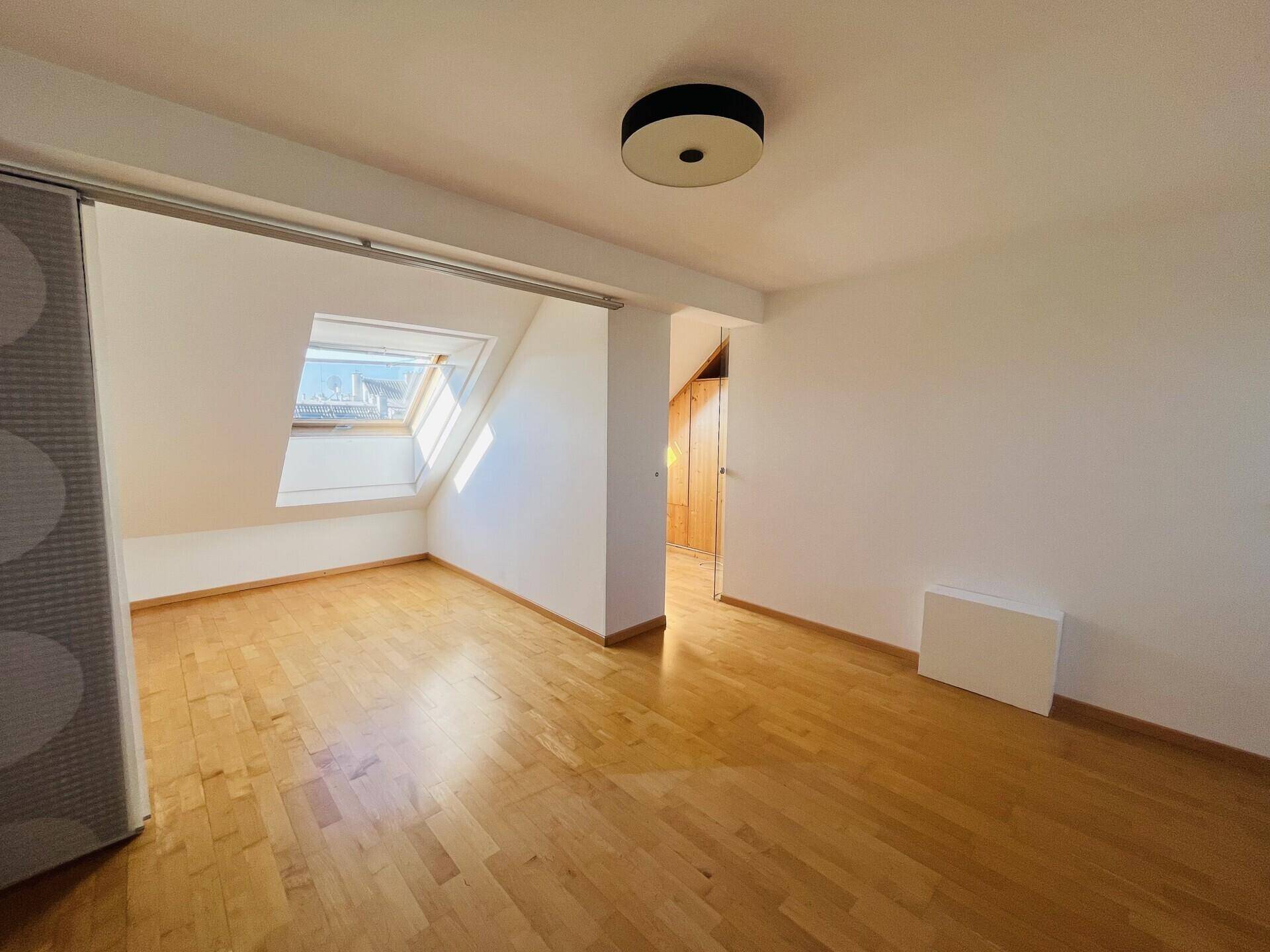 Dachgeschosszimmer mit Holzboden, Dachfenster und viel Tageslicht.
