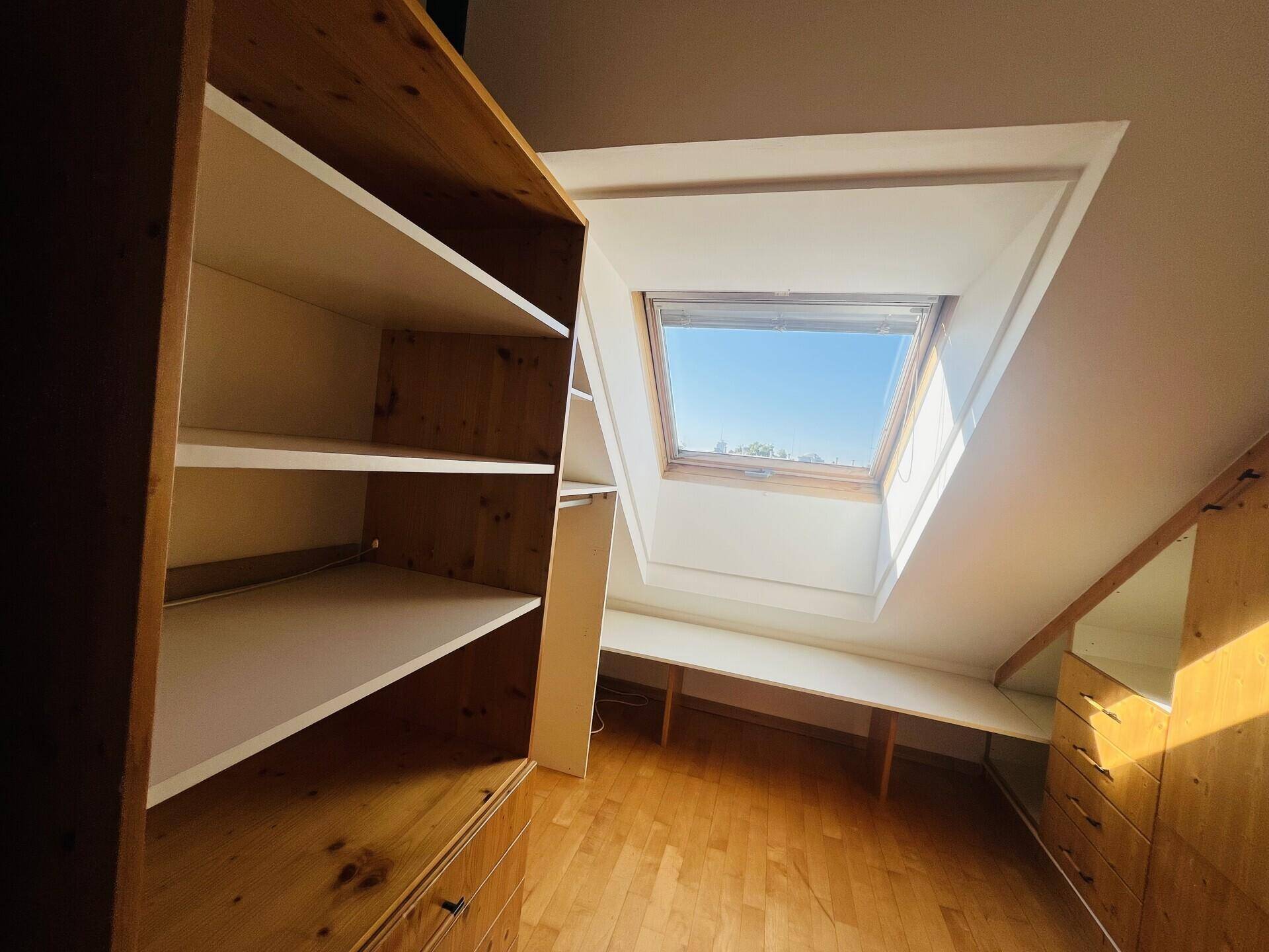 Dachgeschossraum mit Einbauregalen, Holzboden und Dachfenster.