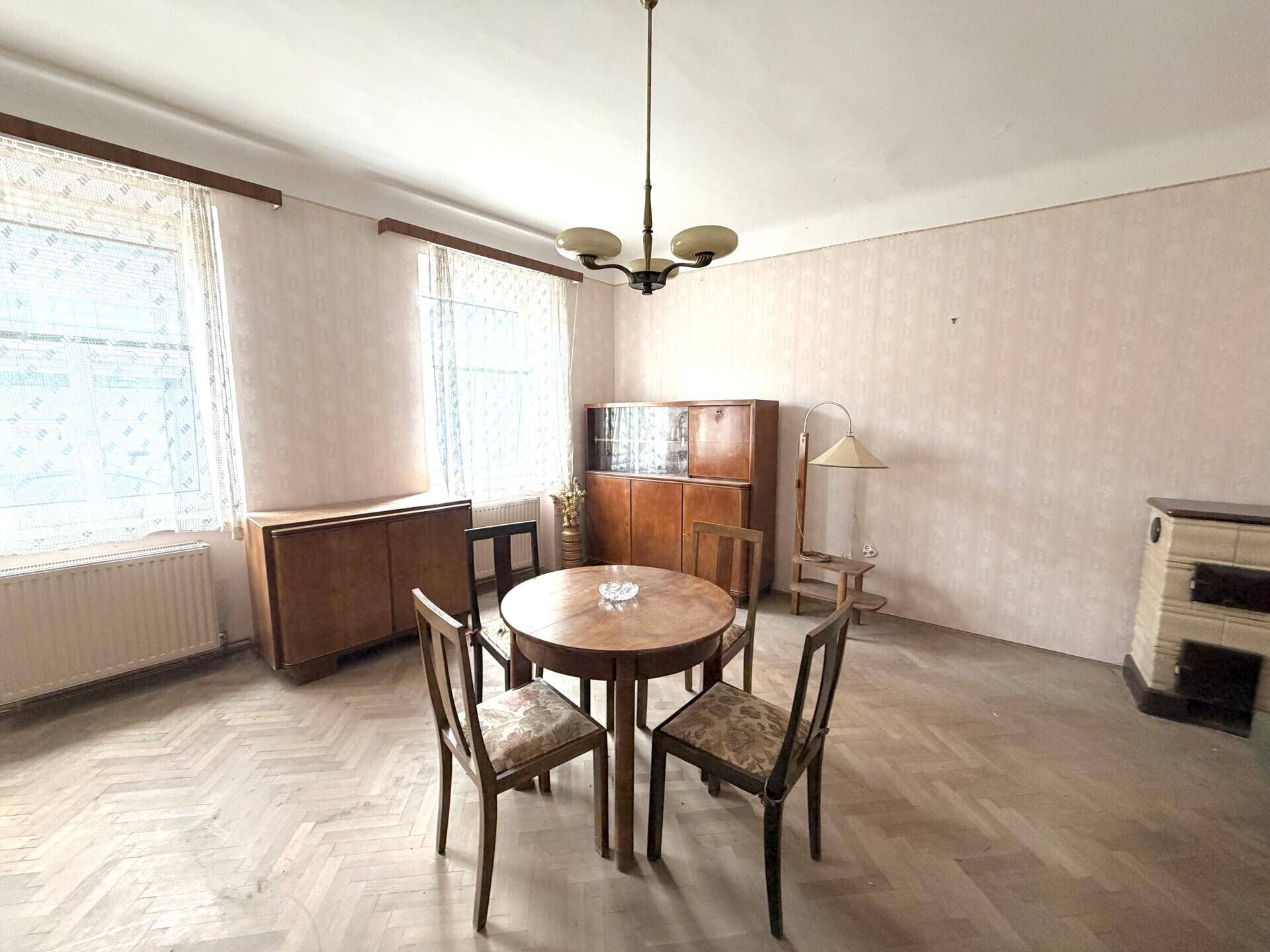 Wohnzimmer mit Fischgrätparkett, einem traditionellen Kachelofen und klassischem Mobiliar.