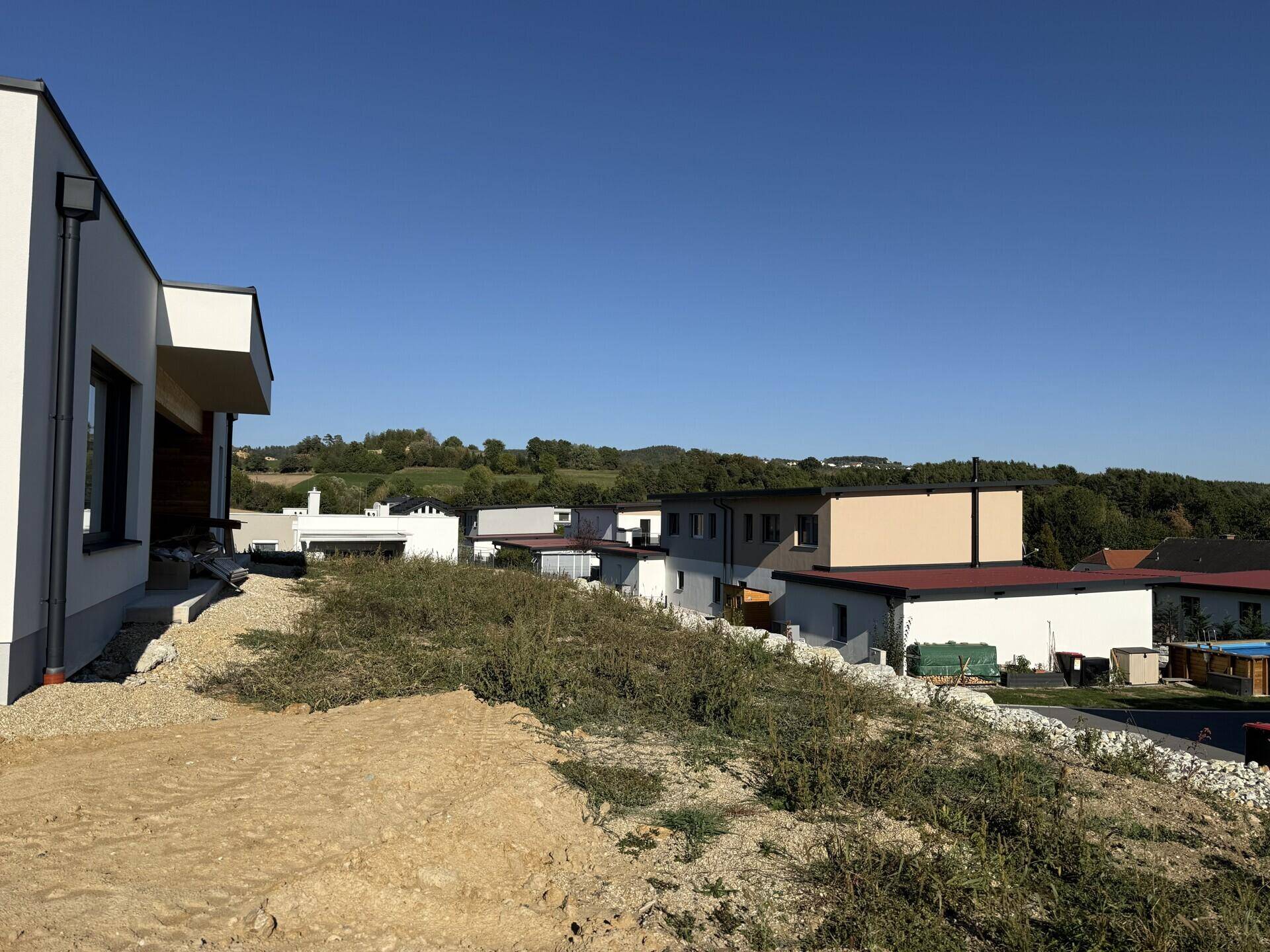 Seitenansicht des Hauses mit Blick auf die umliegende Bebauung und grüne Hügel.