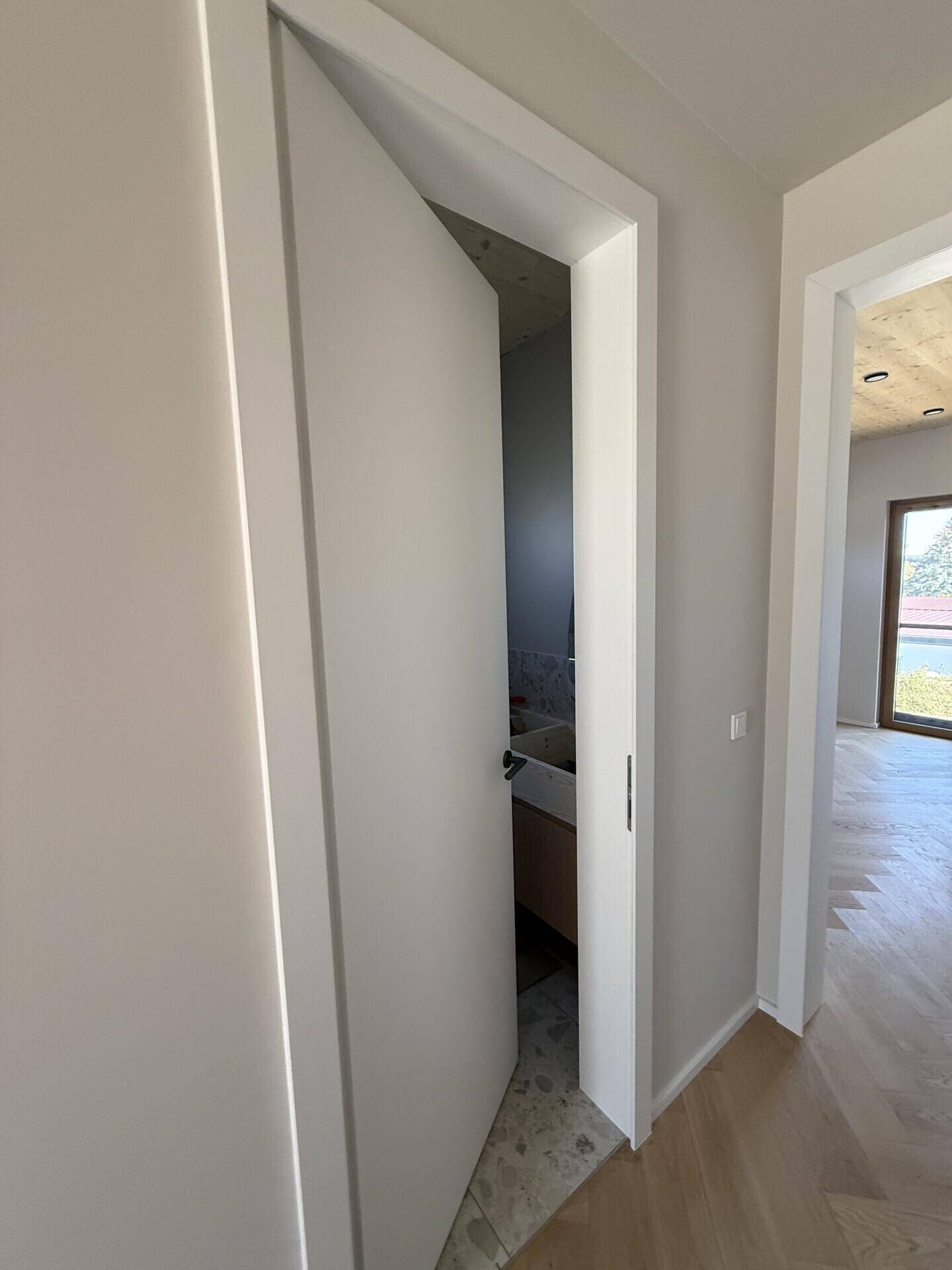 Heller Flur mit Holzboden und einer modernen Tür, die zu einem Badezimmer führt.