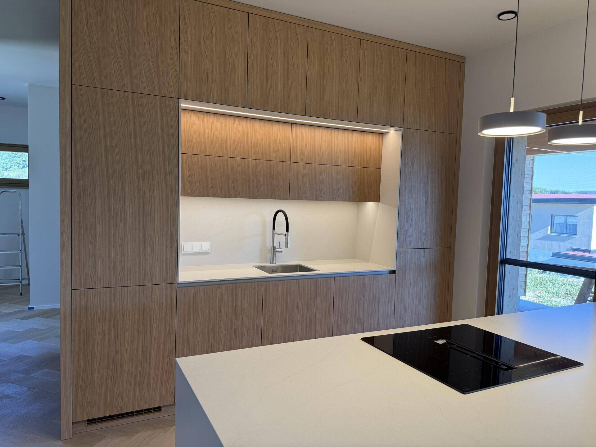 Moderne Holzküche mit Spülbecken, Induktionskochfeld und viel Stauraum.