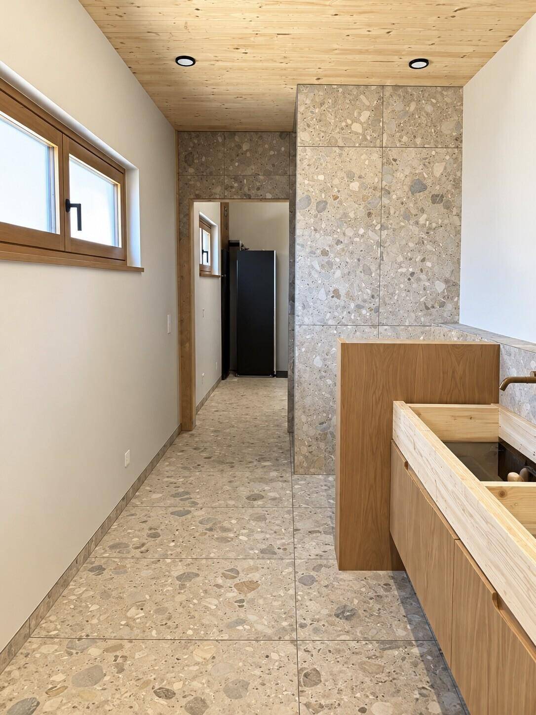 Langer Flur mit Terrazzo-Fliesen und Holzdecke, der zu verschiedenen Räumen führt.