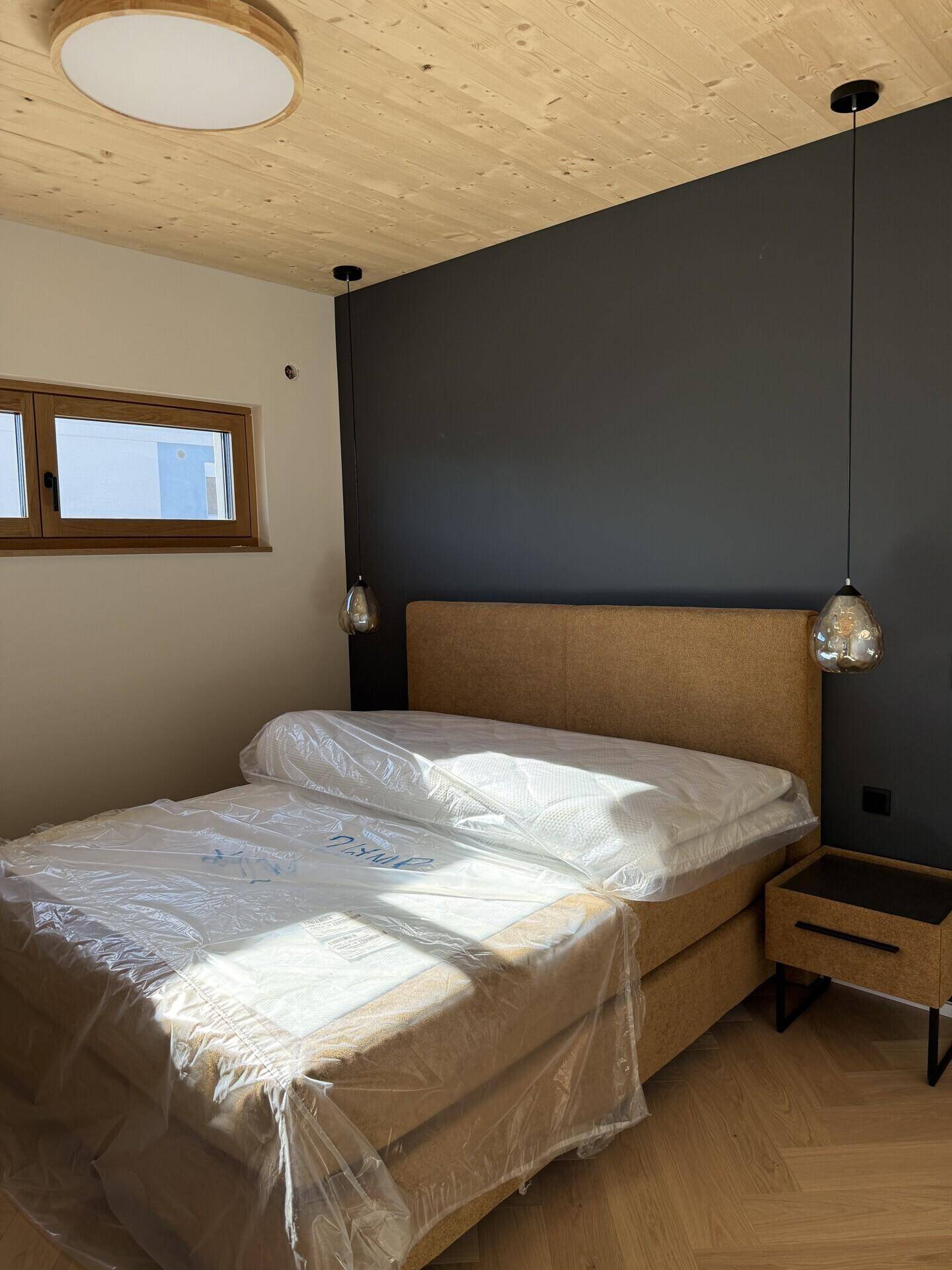 Helles Schlafzimmer mit Holzbalkendecke, Parkettboden und einer dunklen Akzentwand.