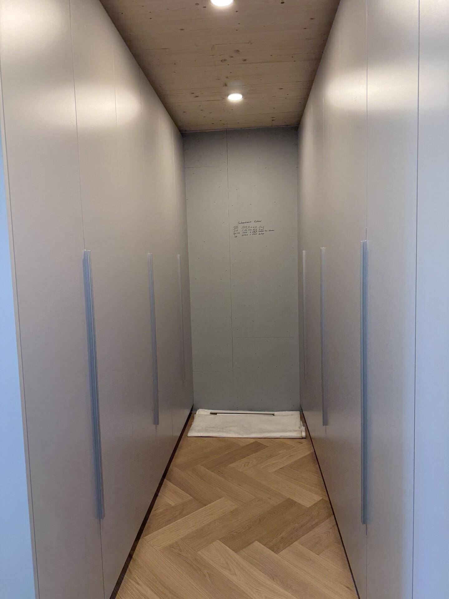 Begehbarer Kleiderschrank mit hellen Einbauschränken und Holzboden.