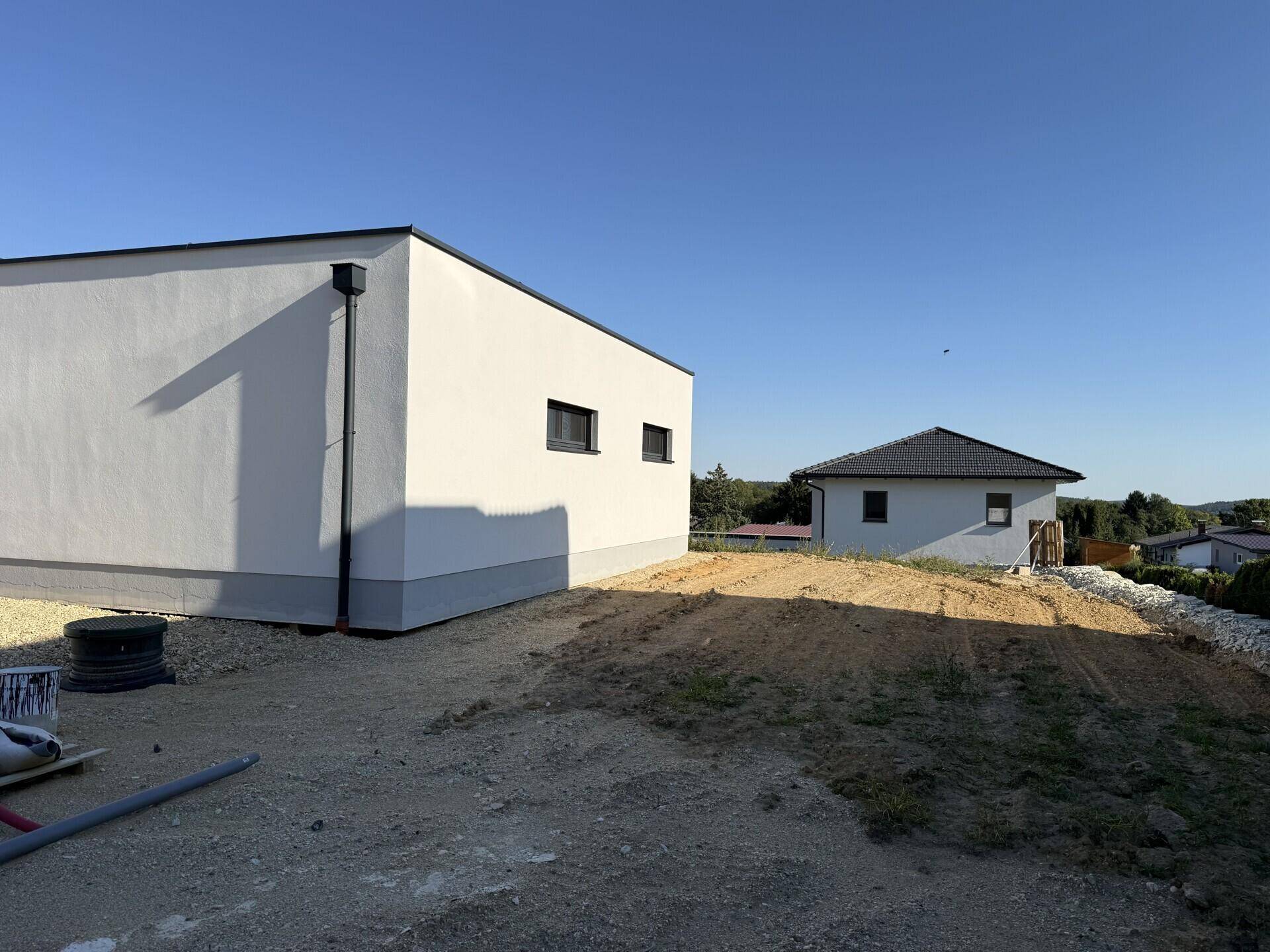 Rückansicht des modernen Hauses mit weißer Fassade und angrenzendem unbebautem Grundstück.