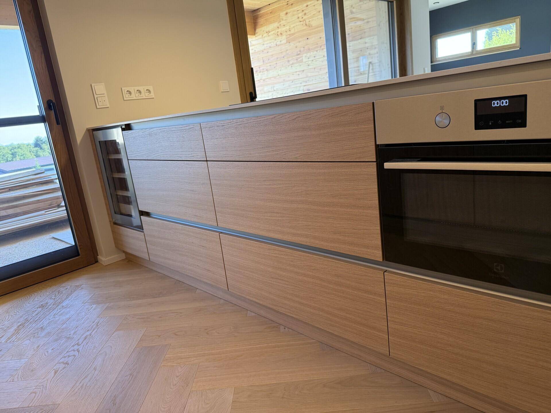 Moderne Holzküche mit integriertem Backofen und Weinkühler, daneben eine Terrassentür.
