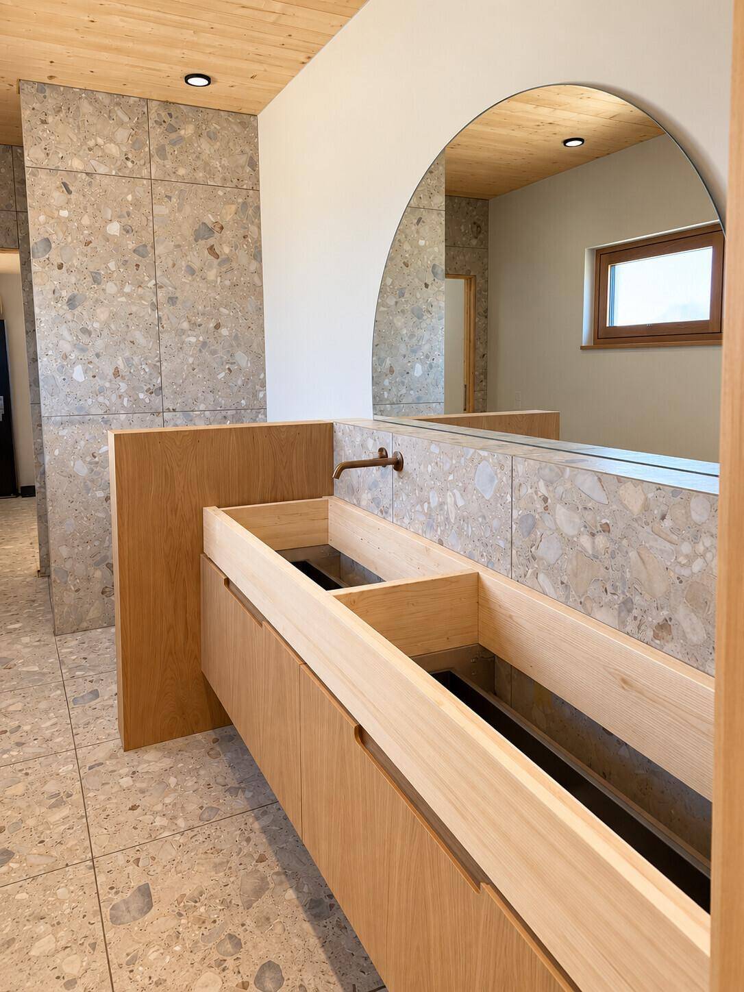 Modernes Badezimmer mit Terrazzo-Fliesen, Holzwaschtisch und großem Rundspiegel.