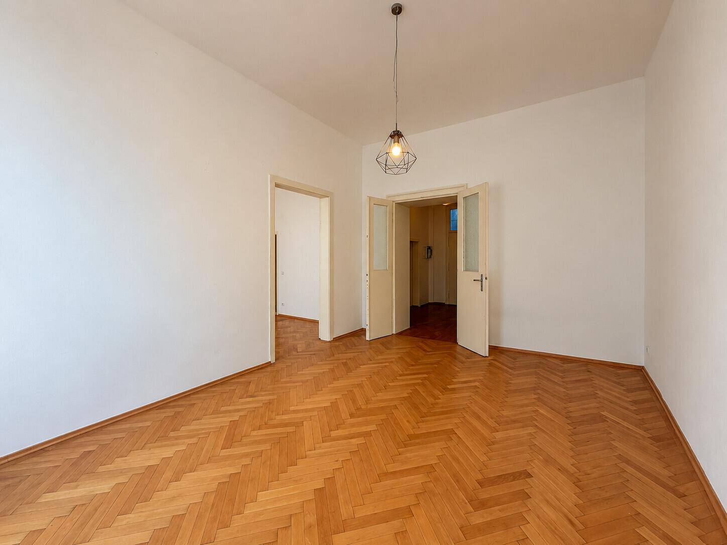 Geräumiges Zimmer mit Fischgrätparkett und Zugang zu weiteren Räumen.