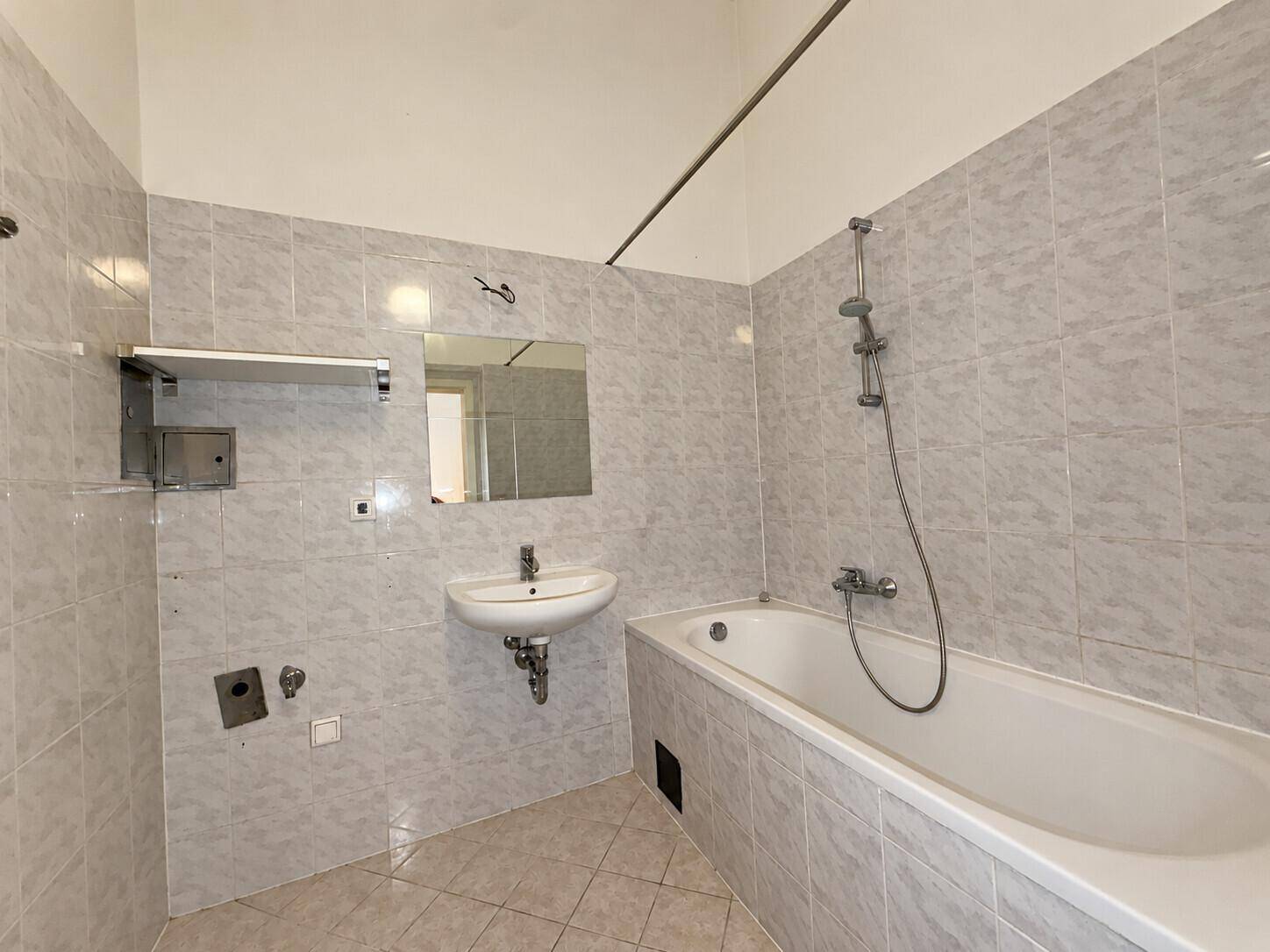Badezimmer mit hellgrauen Fliesen, Badewanne und Waschbecken.