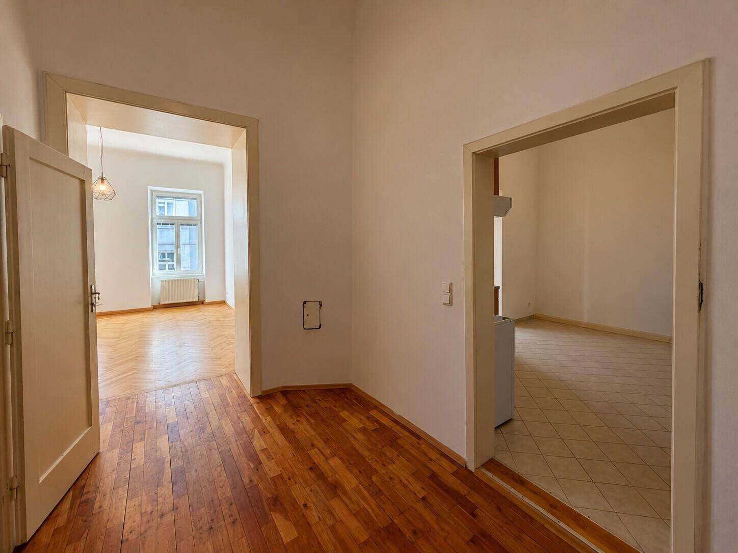 Flur mit Holzboden und Übergang zu einem gefliesten Bereich sowie einem weiteren Zimmer.