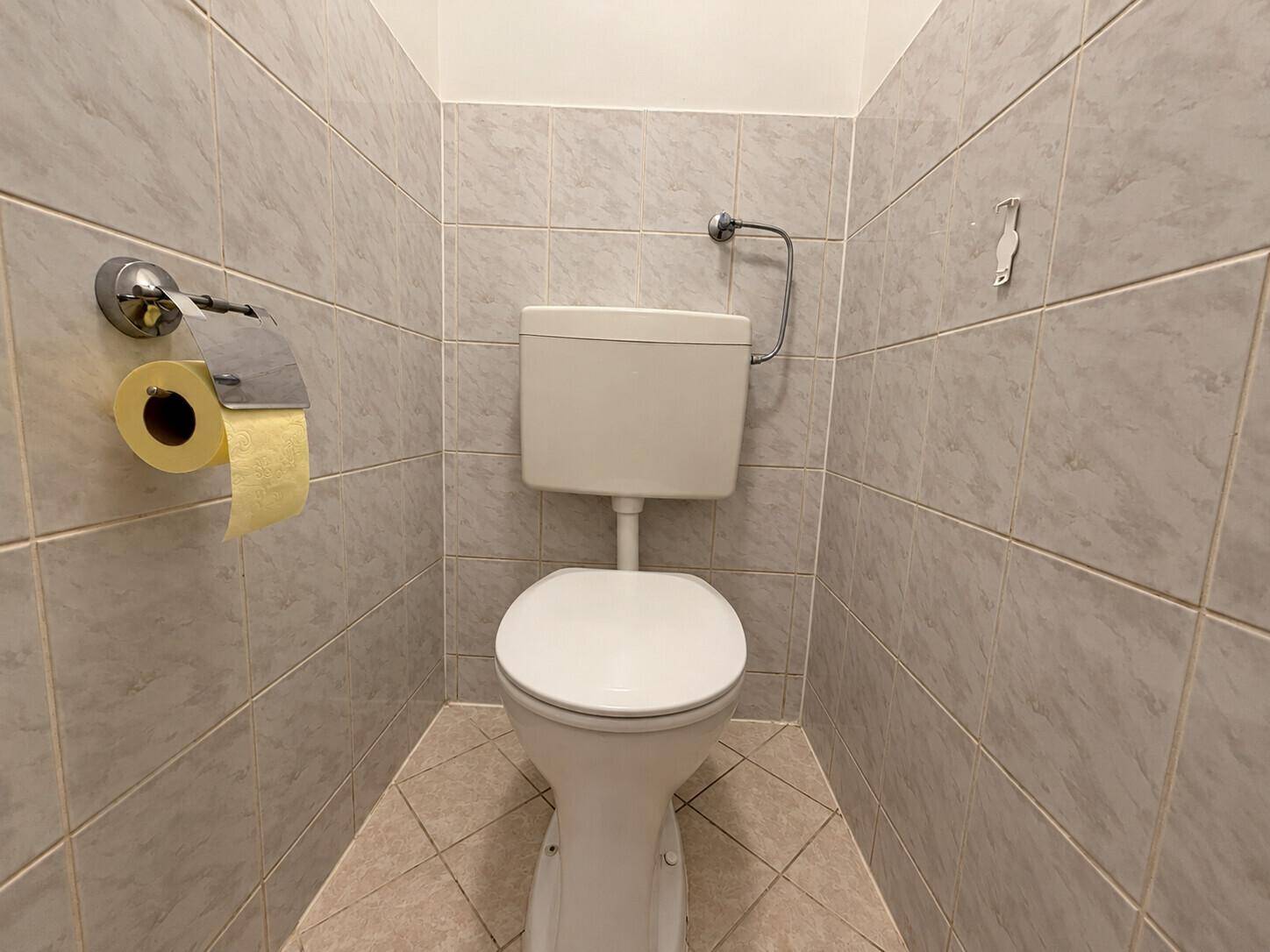 Separate Toilette mit hellgrauen Fliesen und Standard-WC.