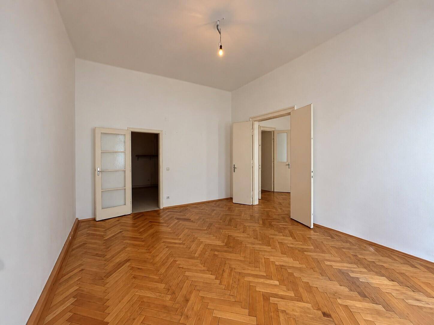 Helles Zimmer mit Fischgrätparkett und mehreren Türen zu angrenzenden Bereichen.