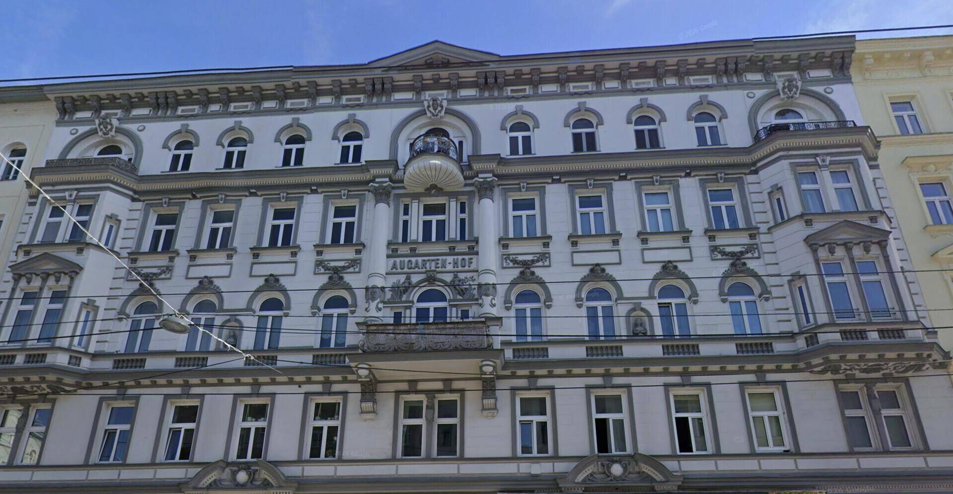 Detailansicht der prunkvollen Fassade des Augarten-Hofs mit Balkon und Stuckverzierungen.