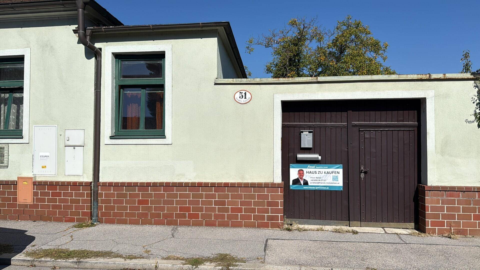 Nahaufnahme der Garagentore eines Hauses mit einem "Haus zu kaufen" Schild.