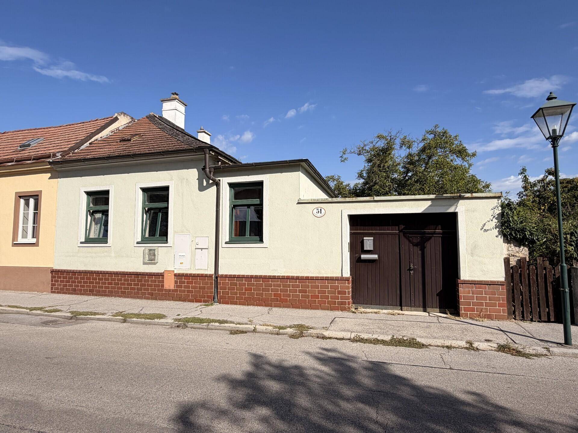 Vorderansicht eines traditionellen Hauses mit Garage und Laterne an einer ruhigen Straße.