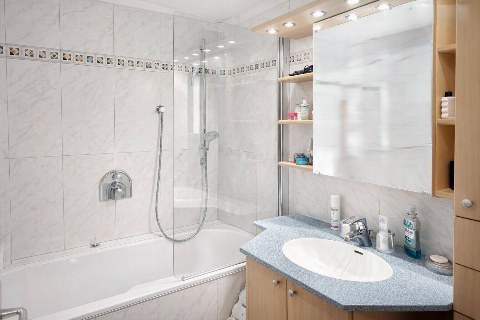 Badezimmer mit Badewanne, Duschvorrichtung, Einzelwaschbecken und Spiegelschrank.