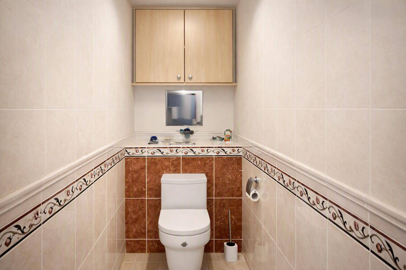Kleines Gäste-WC mit beigen Fliesen, dekorativen Bordüren und einem Hängeschrank.