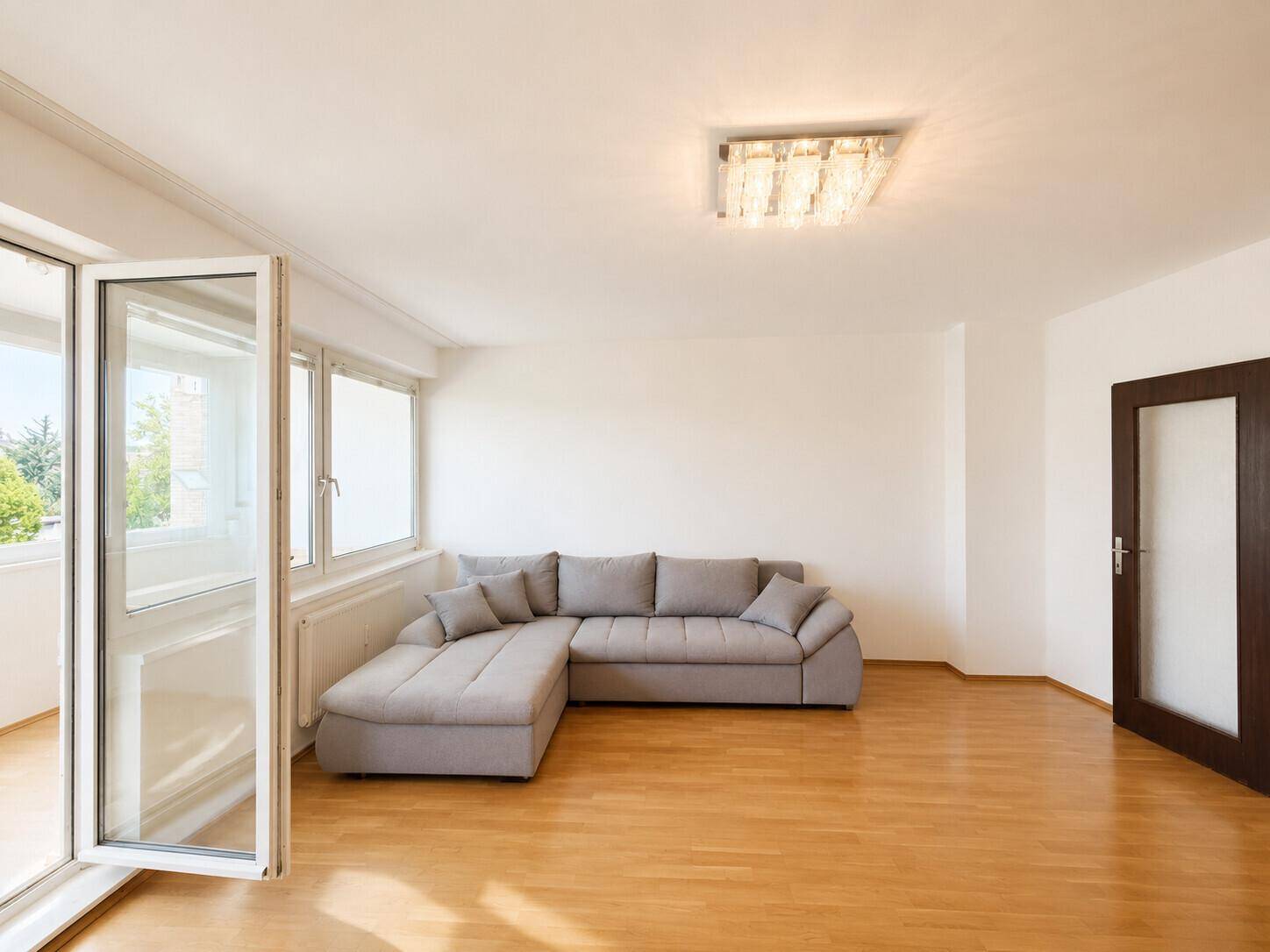 Helles Wohnzimmer mit Parkettboden, modernem Ecksofa und Zugang zur Loggia.
