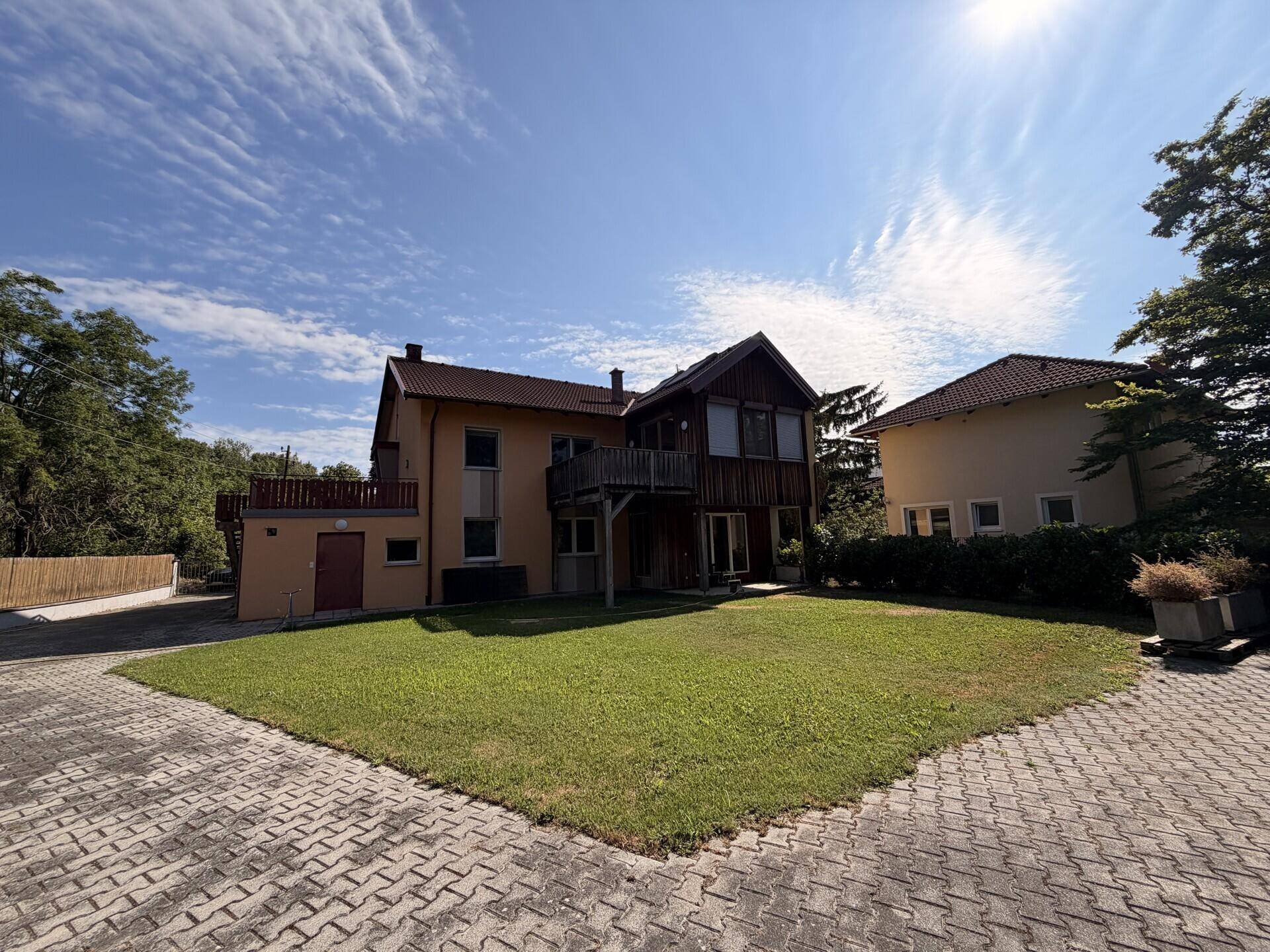 Mehrfamilienhaus mit gepflegtem Rasen und gepflasterter Zufahrt an einem sonnigen Tag.