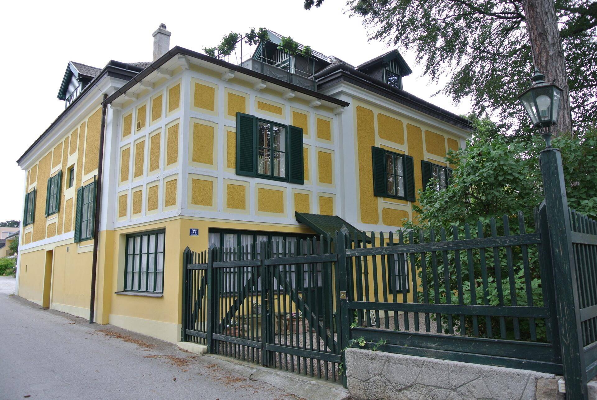 Charmante Villa mit gelb-weißer Fassade, grünen Fensterläden und einem gepflegten Vorgartenbereich.