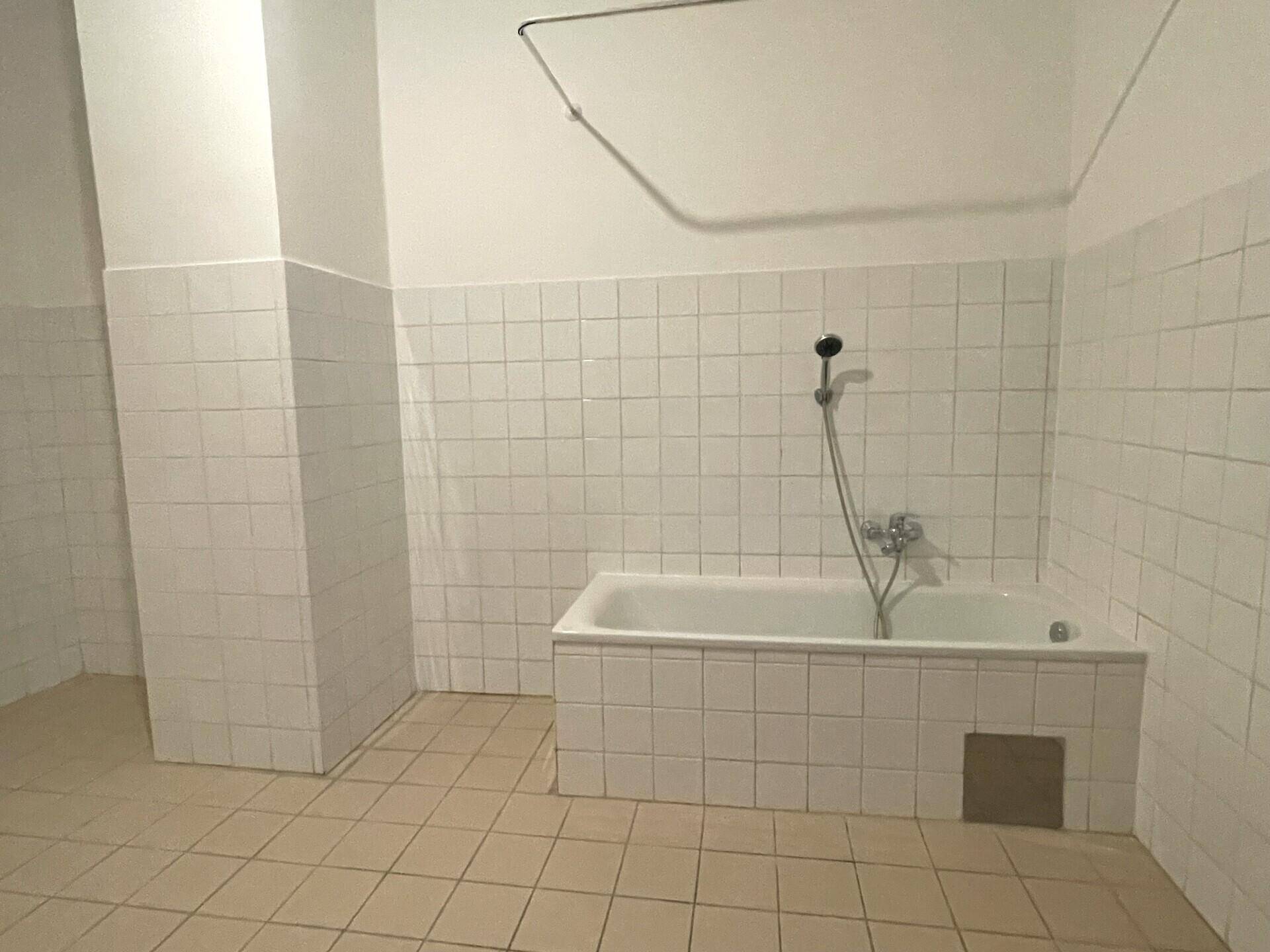 Nahaufnahme der Badewanne und Duscharmatur in einem gefliesten Badezimmer mit beigefarbenem Boden.