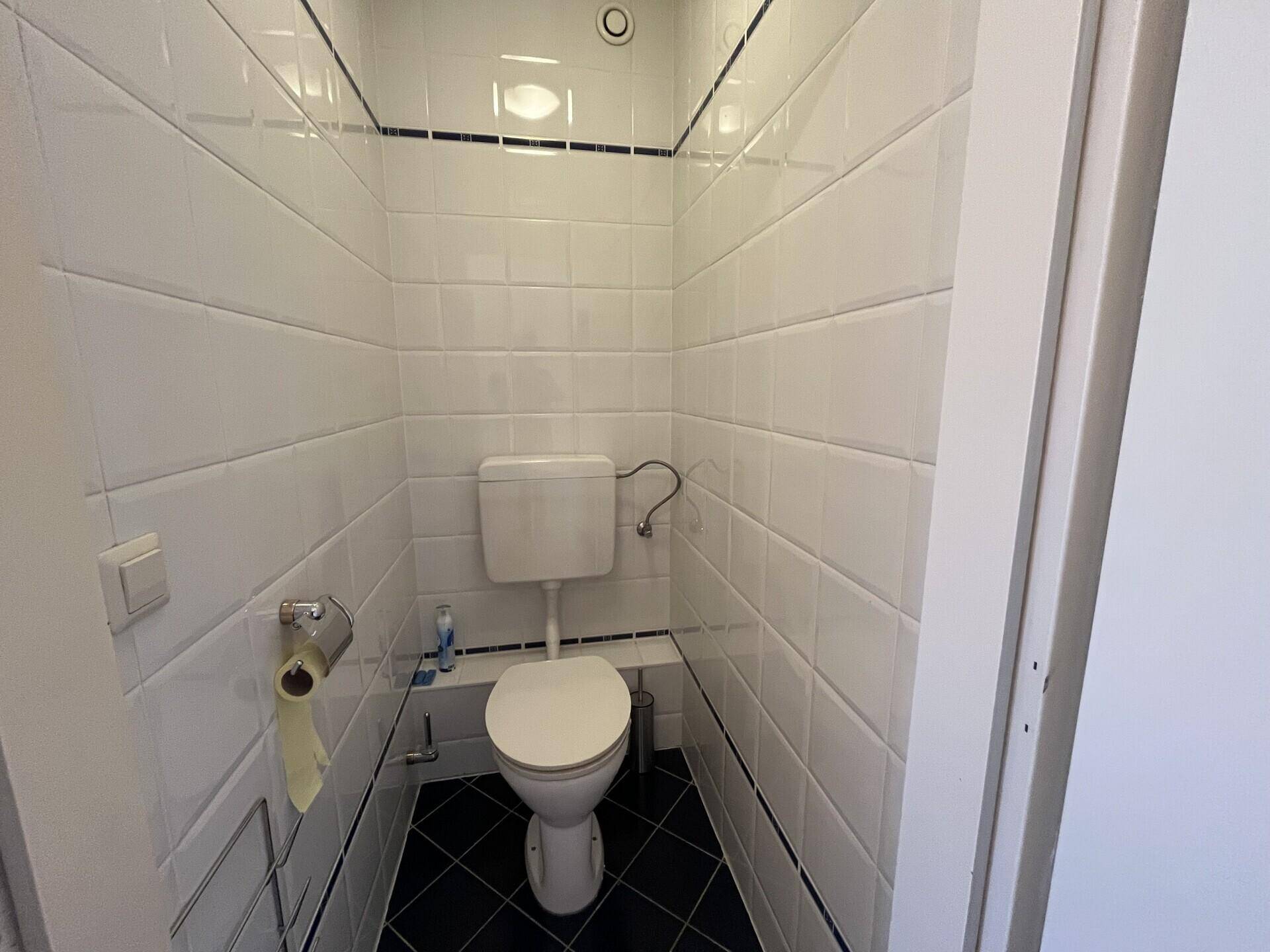 Separates WC mit weißen Wandfliesen und dunklem Boden in kompakter Ausführung.