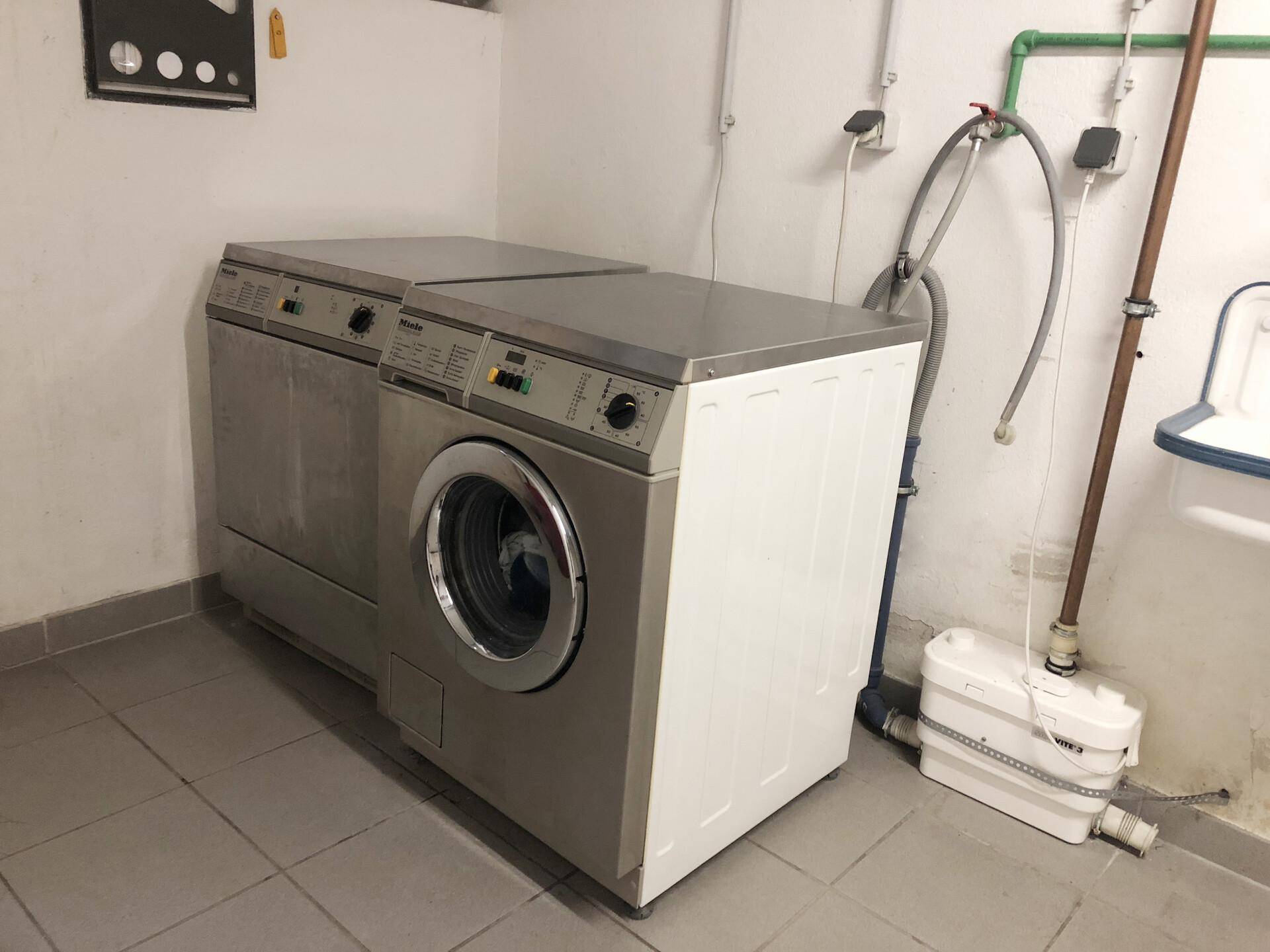 Gemeinschaftlicher Waschraum im Keller mit Waschmaschine, Trockner und gefliestem Boden.