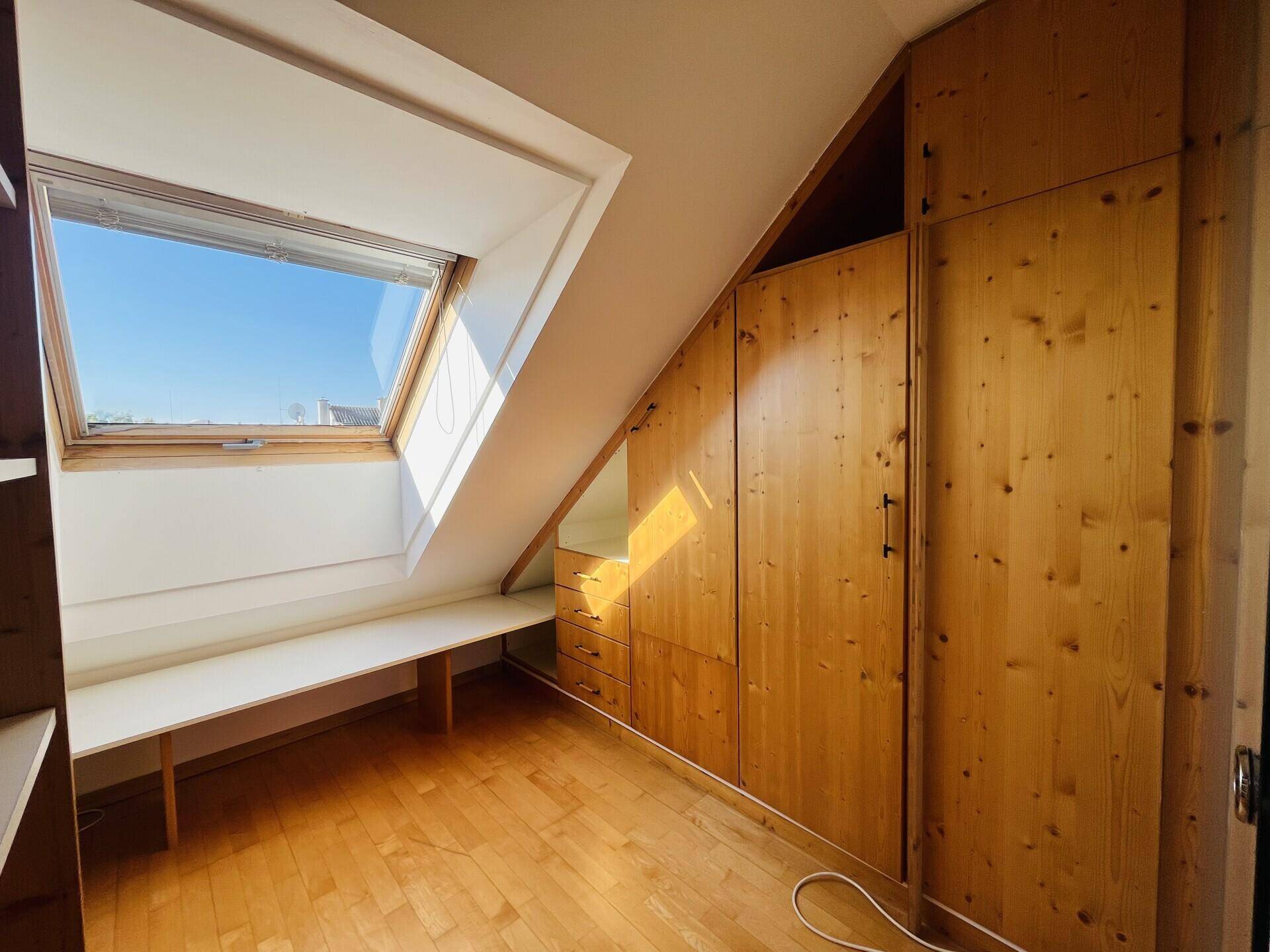 Dachgeschossraum mit Holzboden, Dachfenster und integrierten Holzschränken für Stauraum.