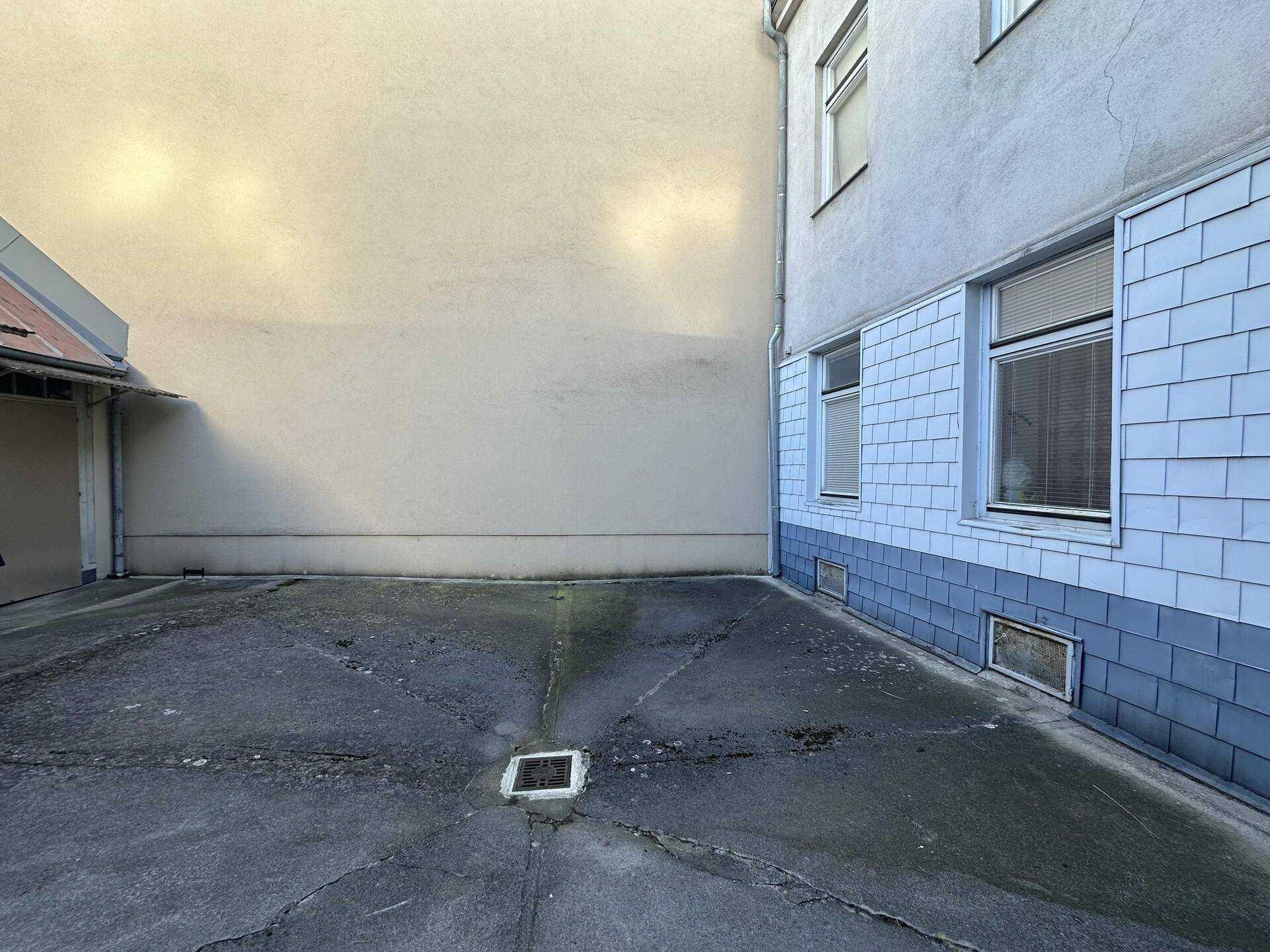 Außenparkplatz in einem Hinterhof zwischen Gebäuden mit grauer Asphaltfläche.