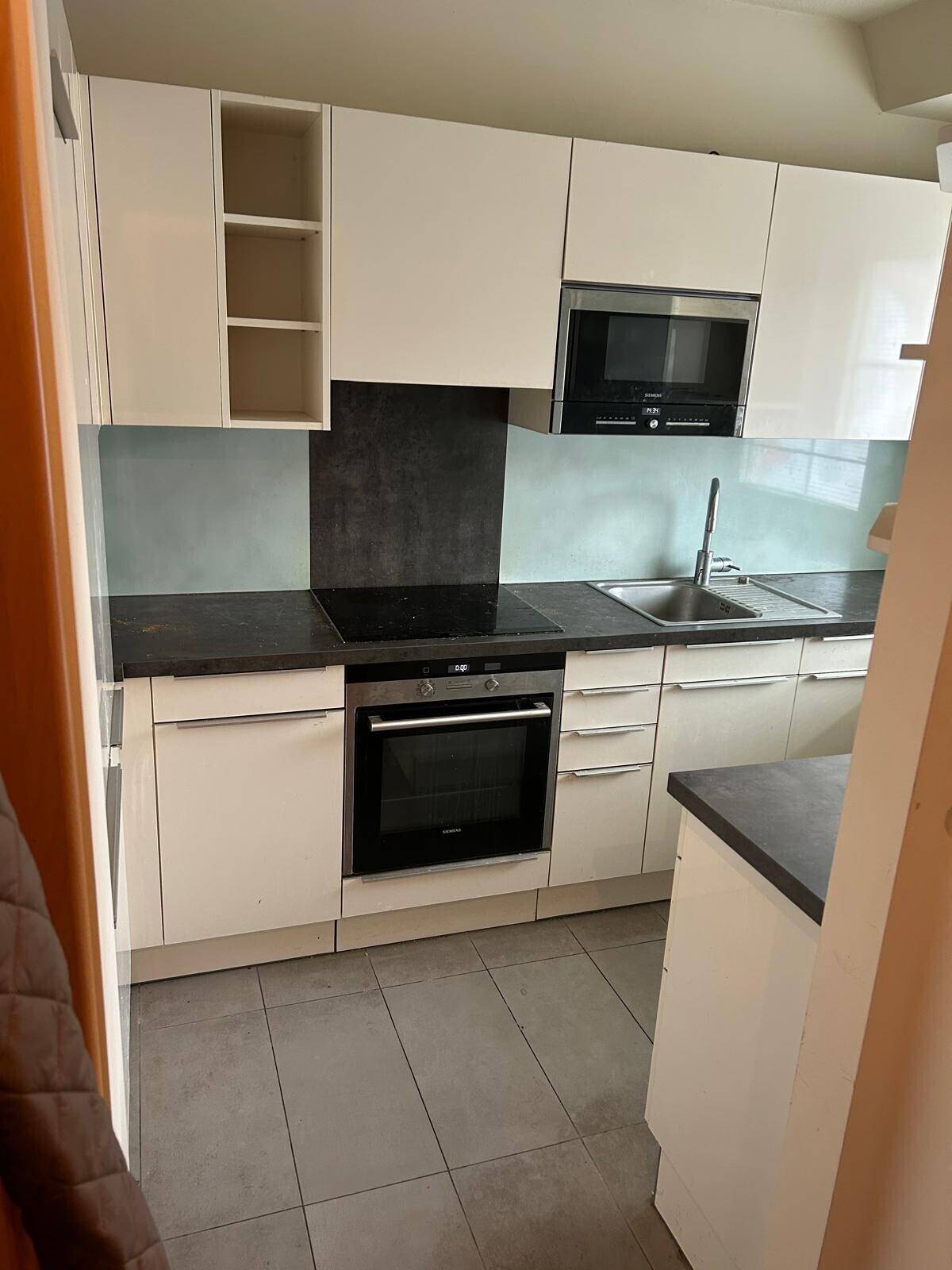 Moderne Küche mit weißen Hochglanzschränken, dunkler Arbeitsplatte und integrierten Geräten.