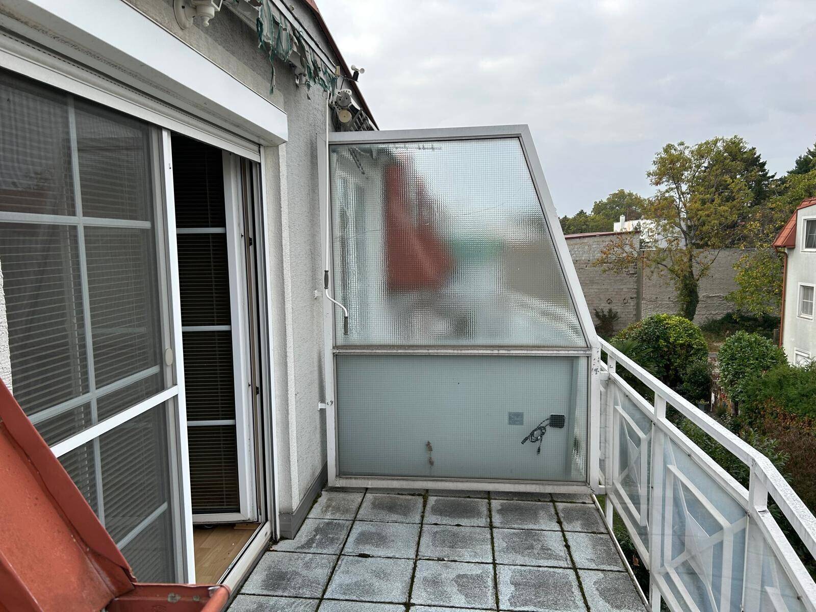 Balkon mit Fliesenboden und einer teilweise verglasten Überdachung, umgeben von einer weißen Brüstung.