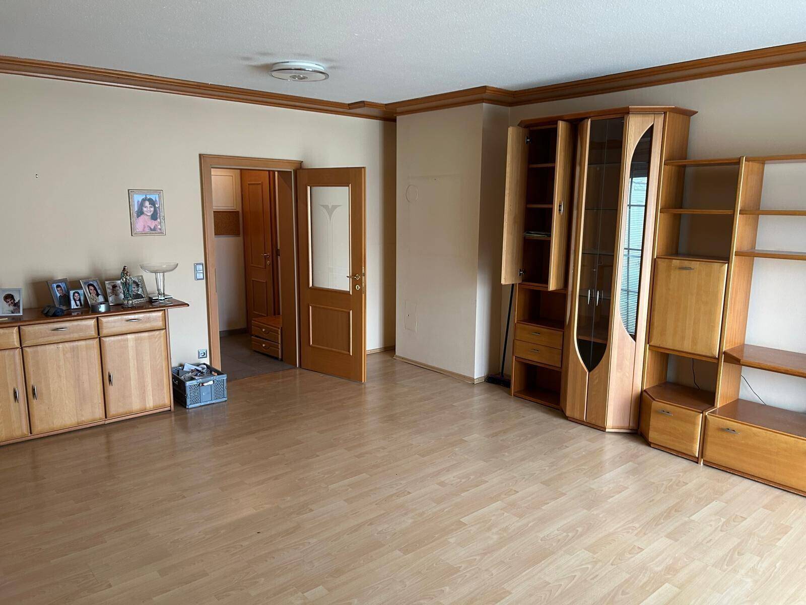 Geräumiges Wohnzimmer mit Holzboden und einer Holzschrankwand, die viel Stauraum bietet.