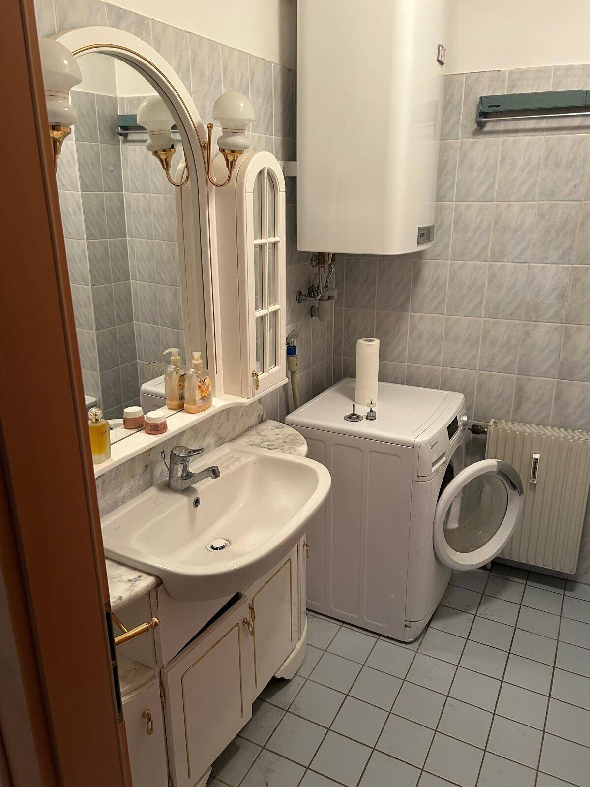 Badezimmer mit Waschbecken, Spiegel, Waschmaschine und hellblauen Fliesen an Wänden und Boden.
