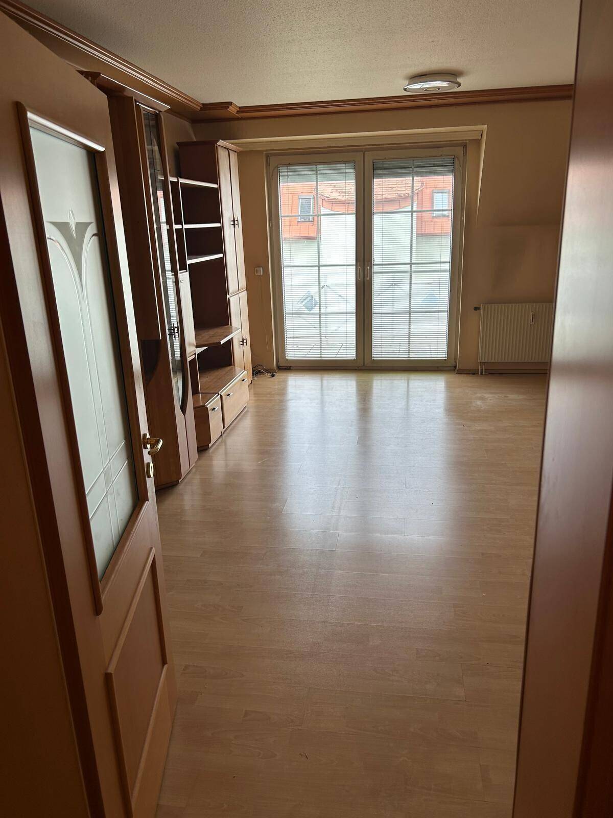 Wohnzimmer mit Holzboden und einer großen Fenstertür, die viel Tageslicht hereinlässt.