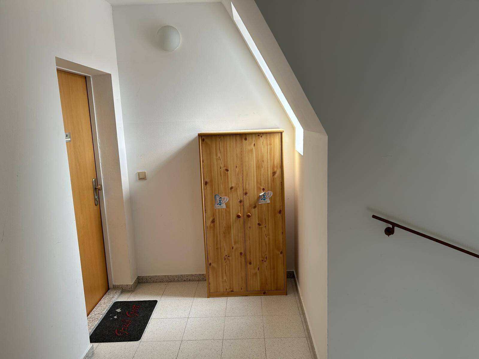 Heller Flur mit Fliesenboden, einer Holztür und einer Dachschräge, die den Raum prägt.