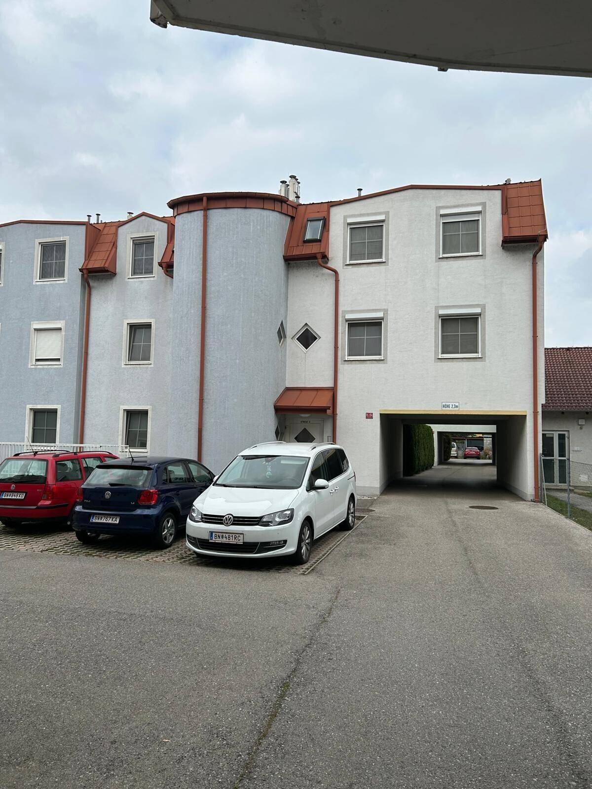 Mehrfamilienhaus mit verschiedenen Fassadenfarben und einem Durchgang zum Innenhof oder weiteren Parkplätzen.